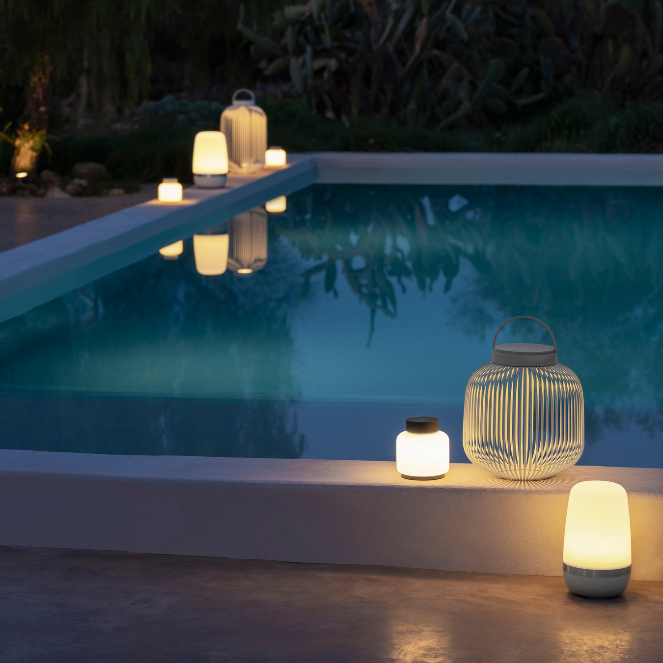 FAWN, SPIRIT and LITO Lanterns lit at night placed by a swimming pool.