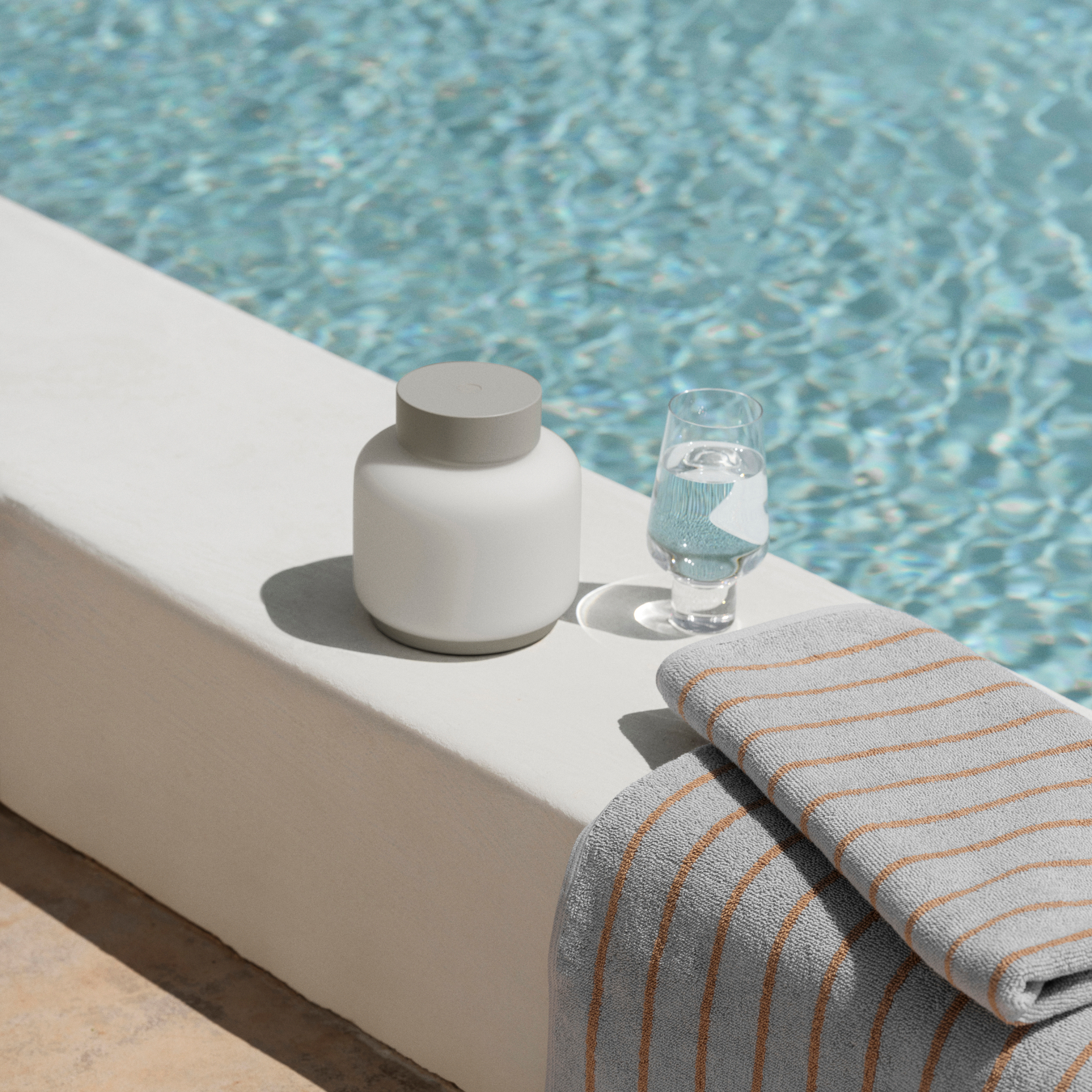 FAWN Lantern unlit sitting by a swimming pool with a KOYOI Glass filled with water and a beach towel.