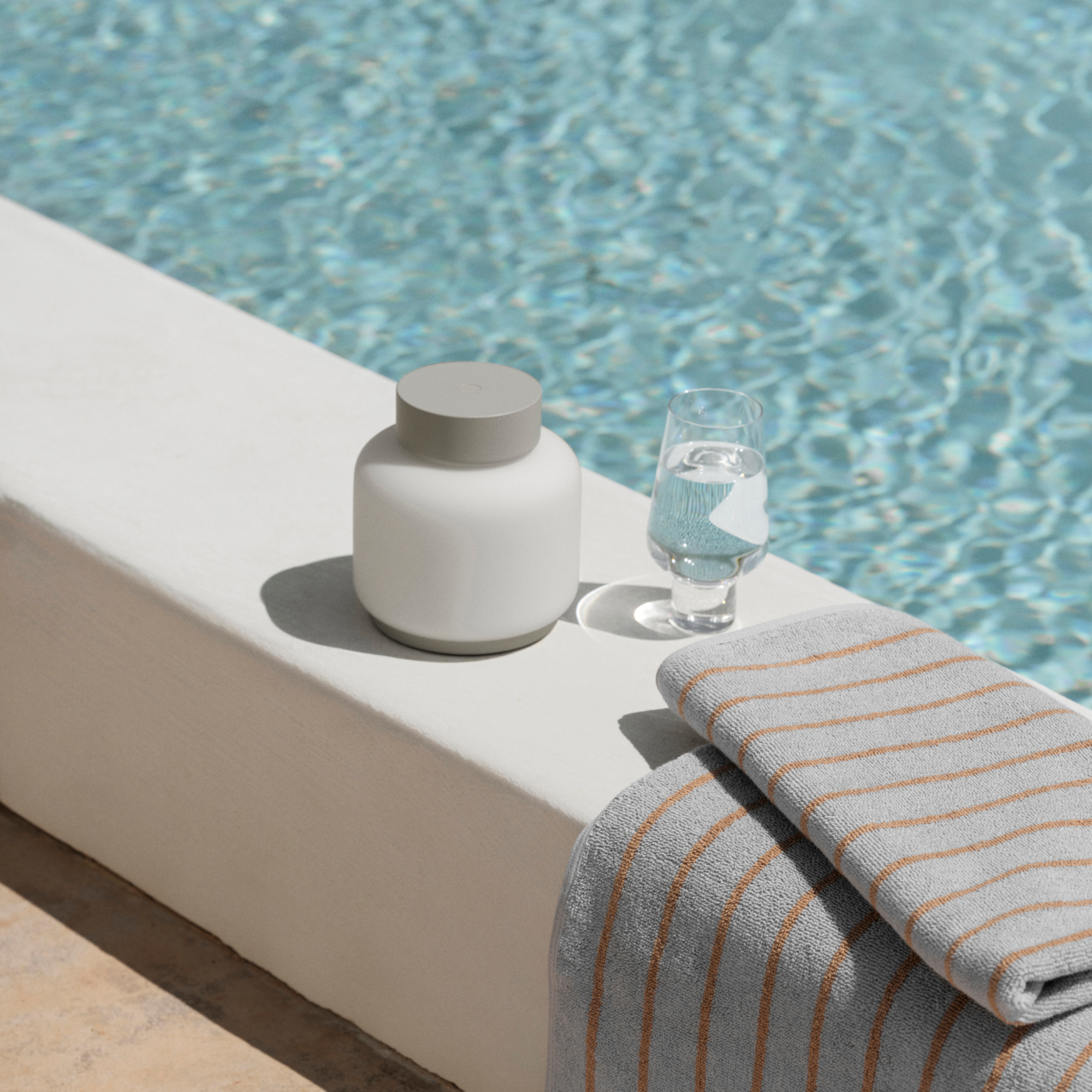 FAWN Lantern unlit sitting by a swimming pool with a KOYOI Glass filled with water and a beach towel.