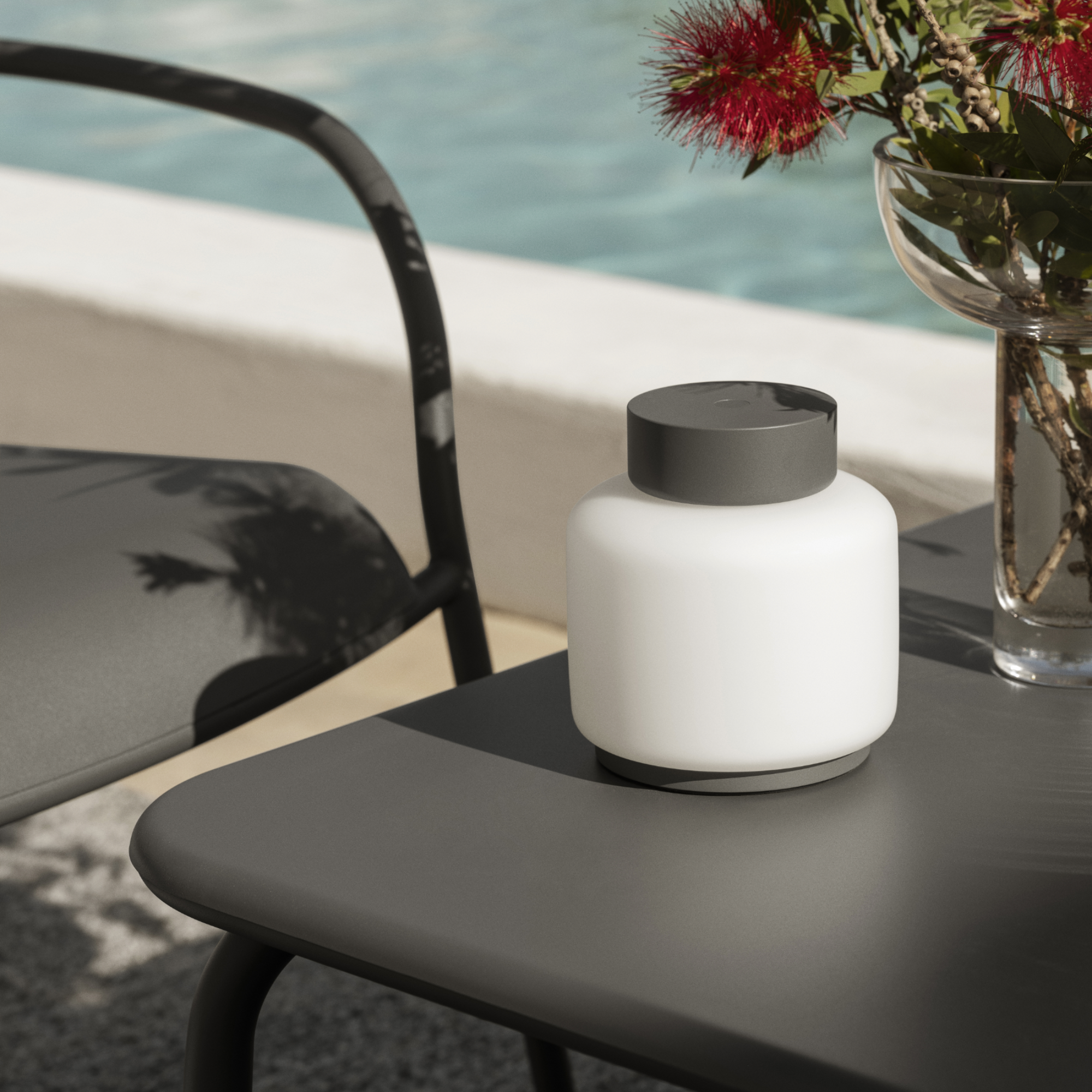 FAWN Outdoor Lantern sitting on a patio table by a swimming pool. Glass MIYABI Vase also on the patio table.