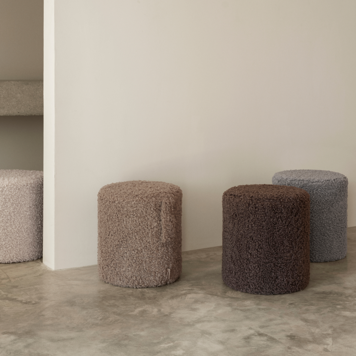 Four Teddy Pouf in neutral tones, displayed in a minimalist interior setting with a concrete floor and a light beige wall.