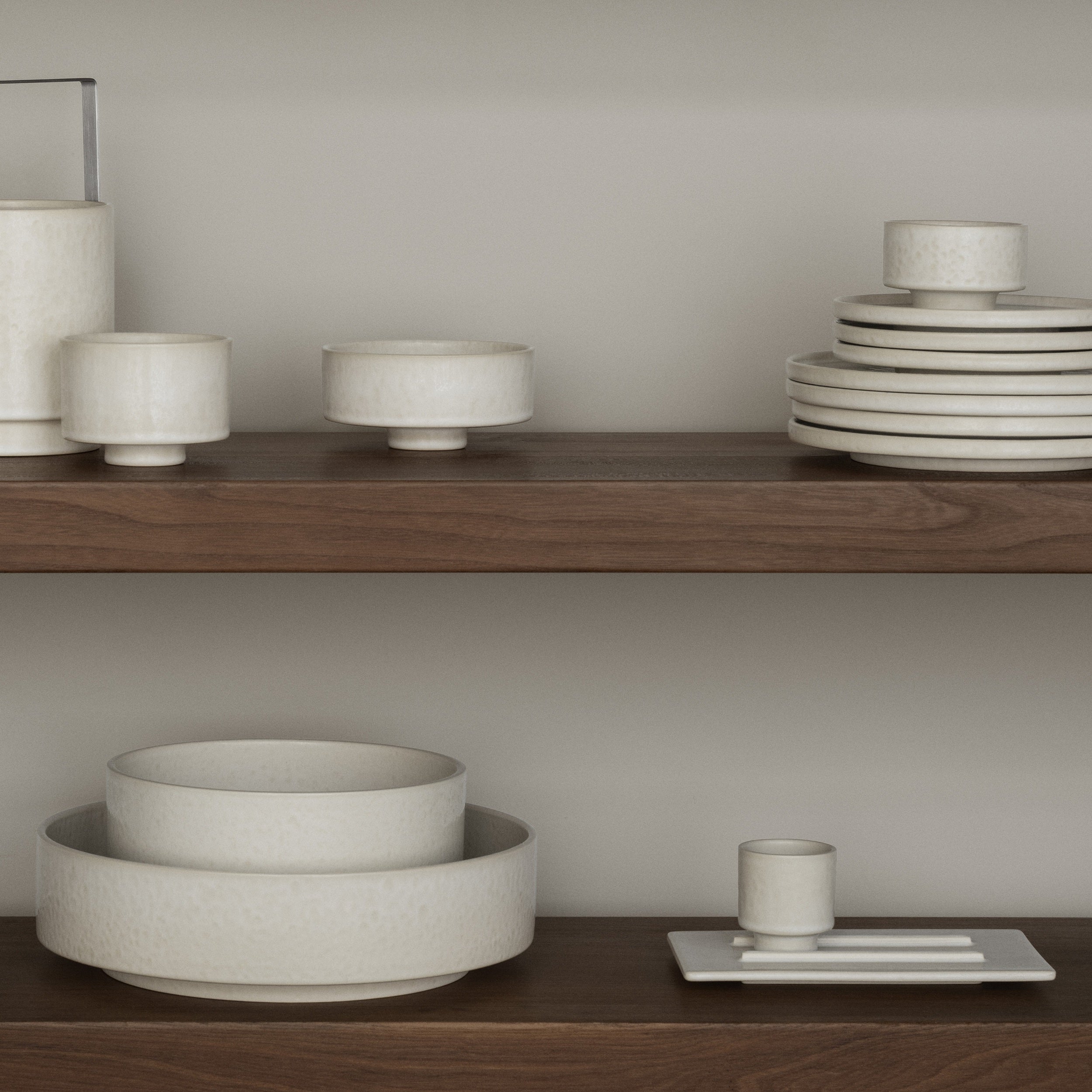 Set of ceramic bowls and plates on wooden shelves against a neutral wall.