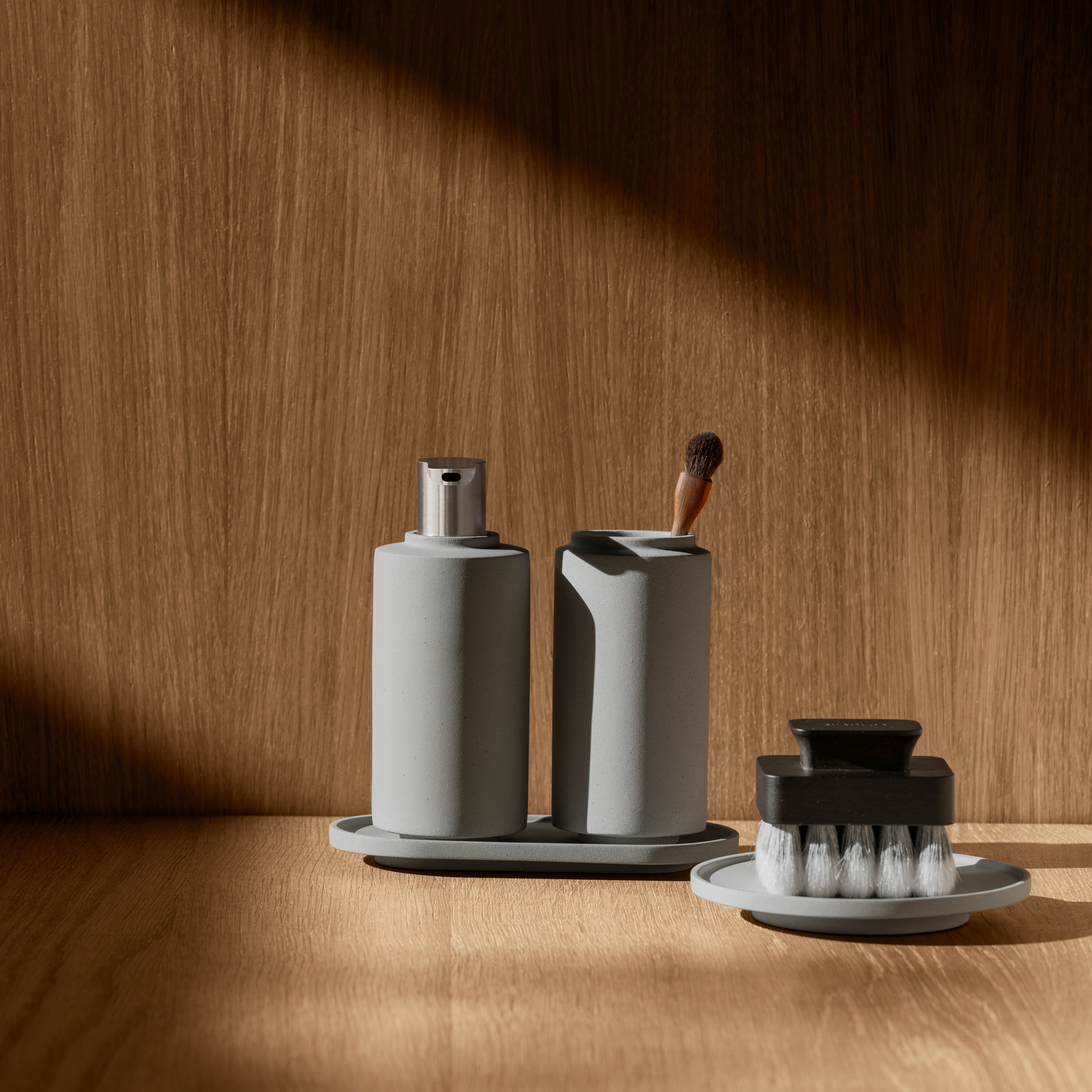Wooden wall and counter with natural light shining in upon CRETO concrete bathroom soap dispenser, tumbler, and tray