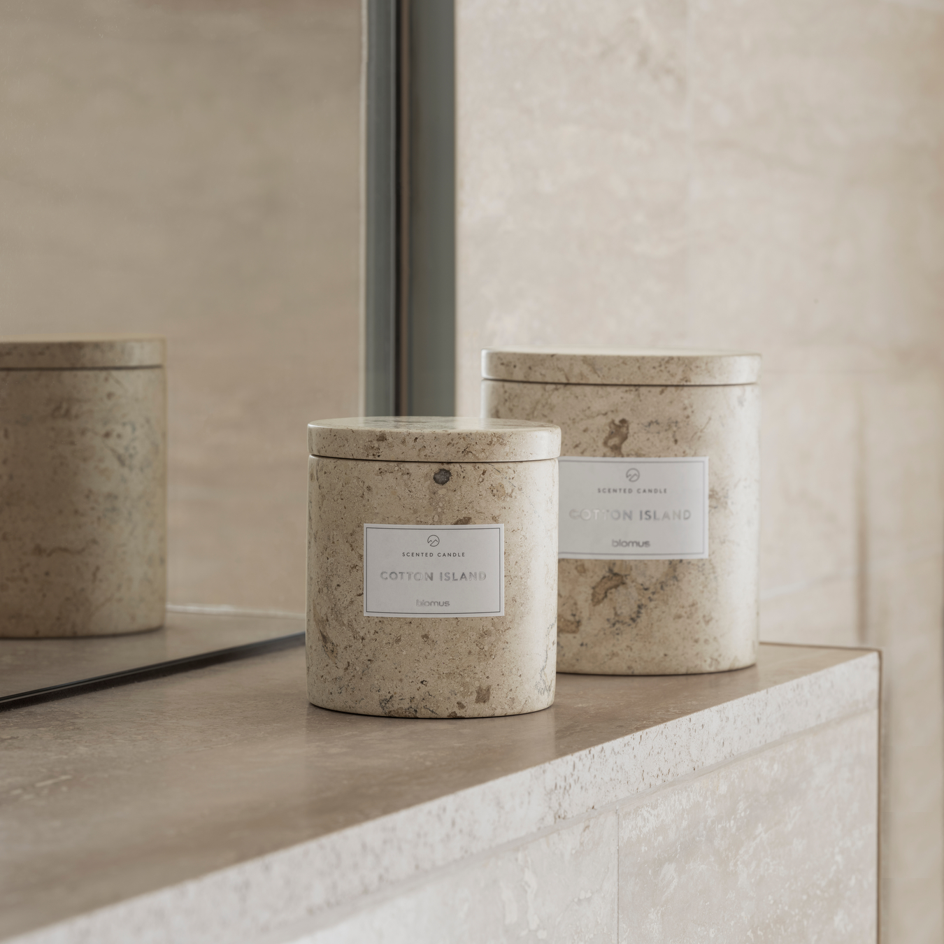 scented soy candles in travertine containers displayed on a marble ledge by a mirror