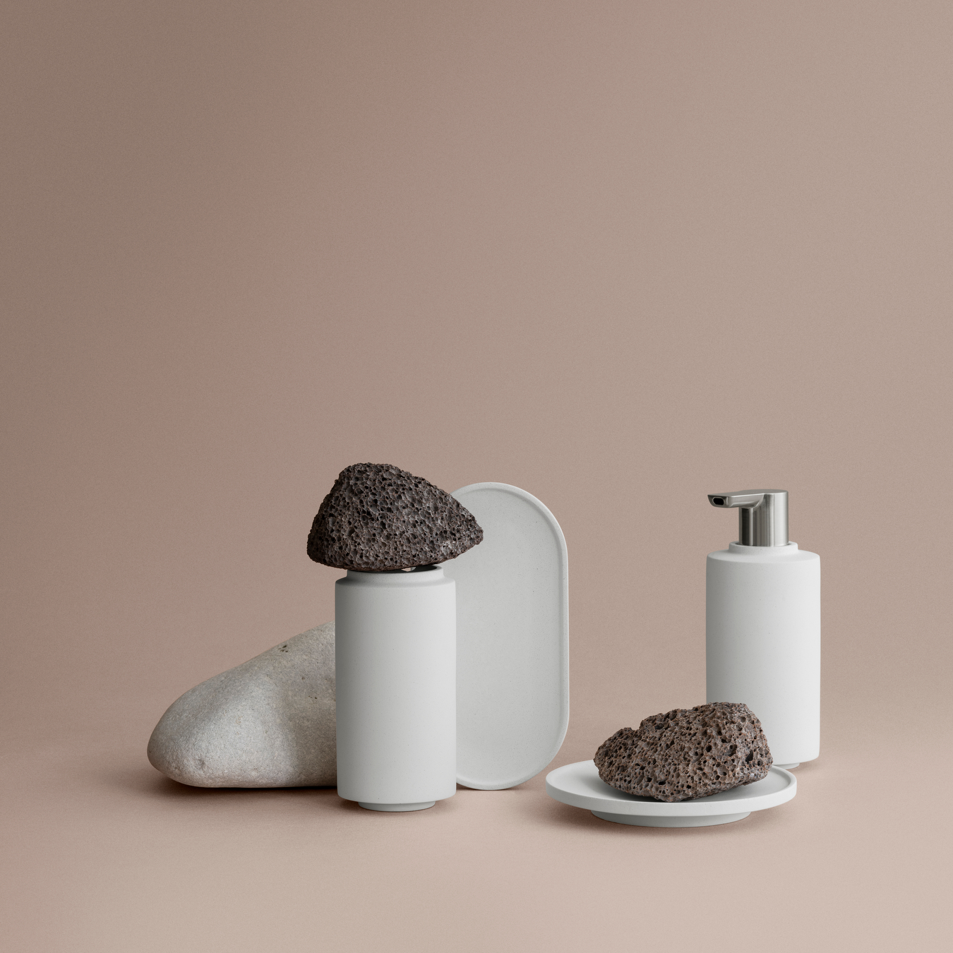 modern minimalist bathroom set displayed against a simple coral pink background with pumice stones arranged for an artistic touch