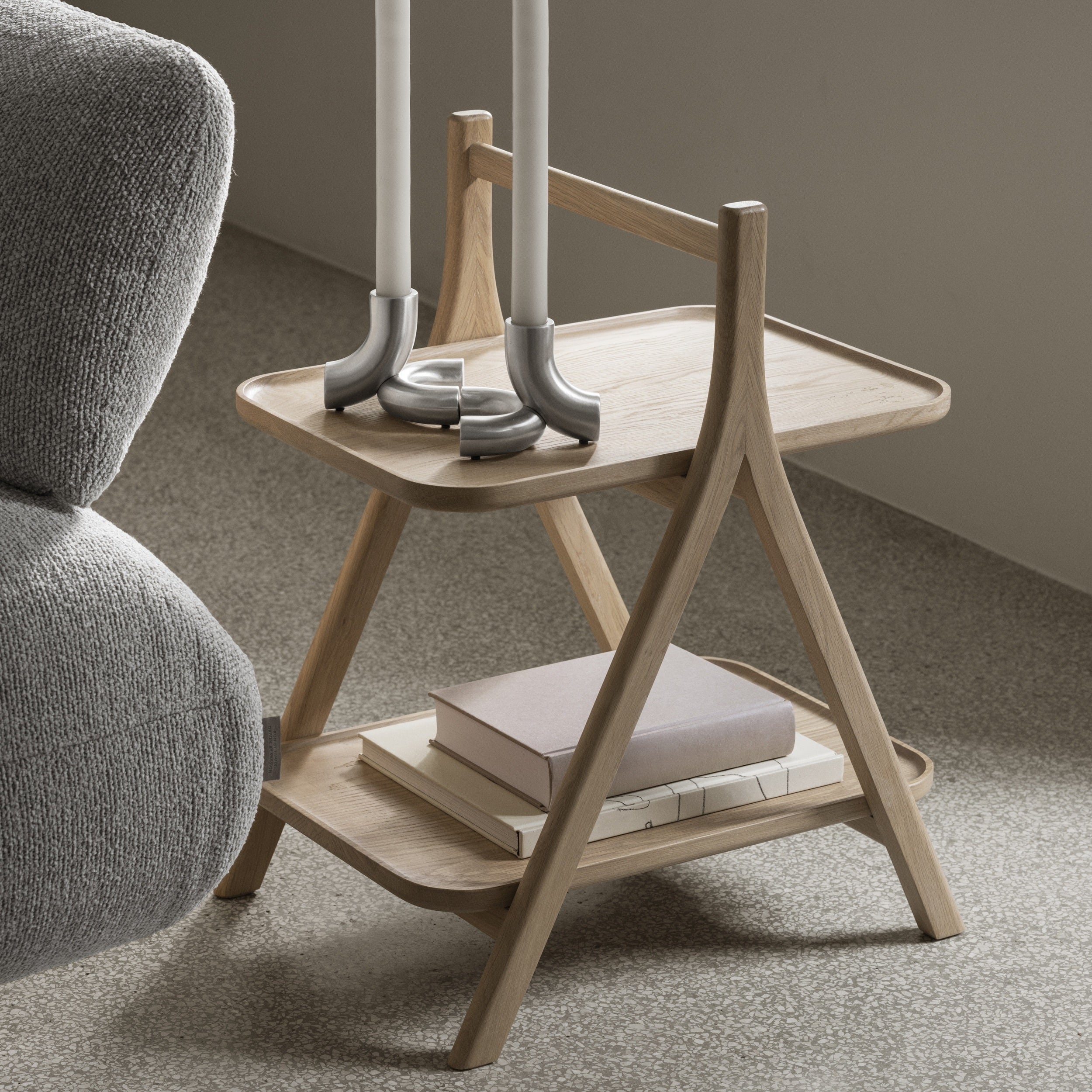 Wooden side table with books and candle holders next to a gray armchair.