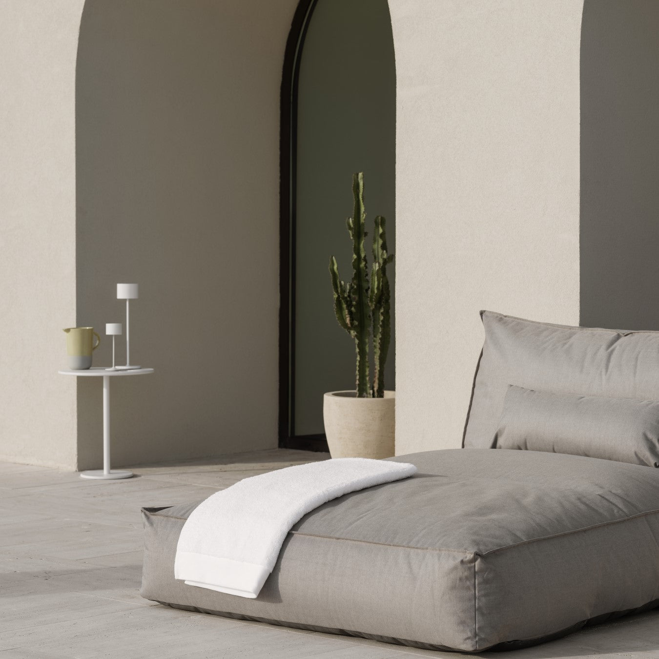 Mediterranean inspired outdoor lounge area with two led lamps on a side table next to a pitcher