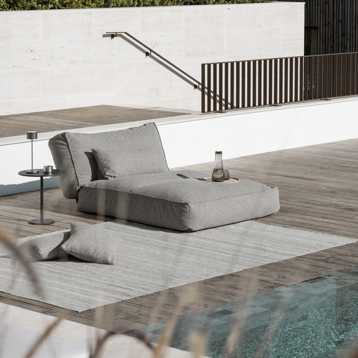 Outdoor lounge area with comfy sofa placed on an outdoor rug near a swimming pool