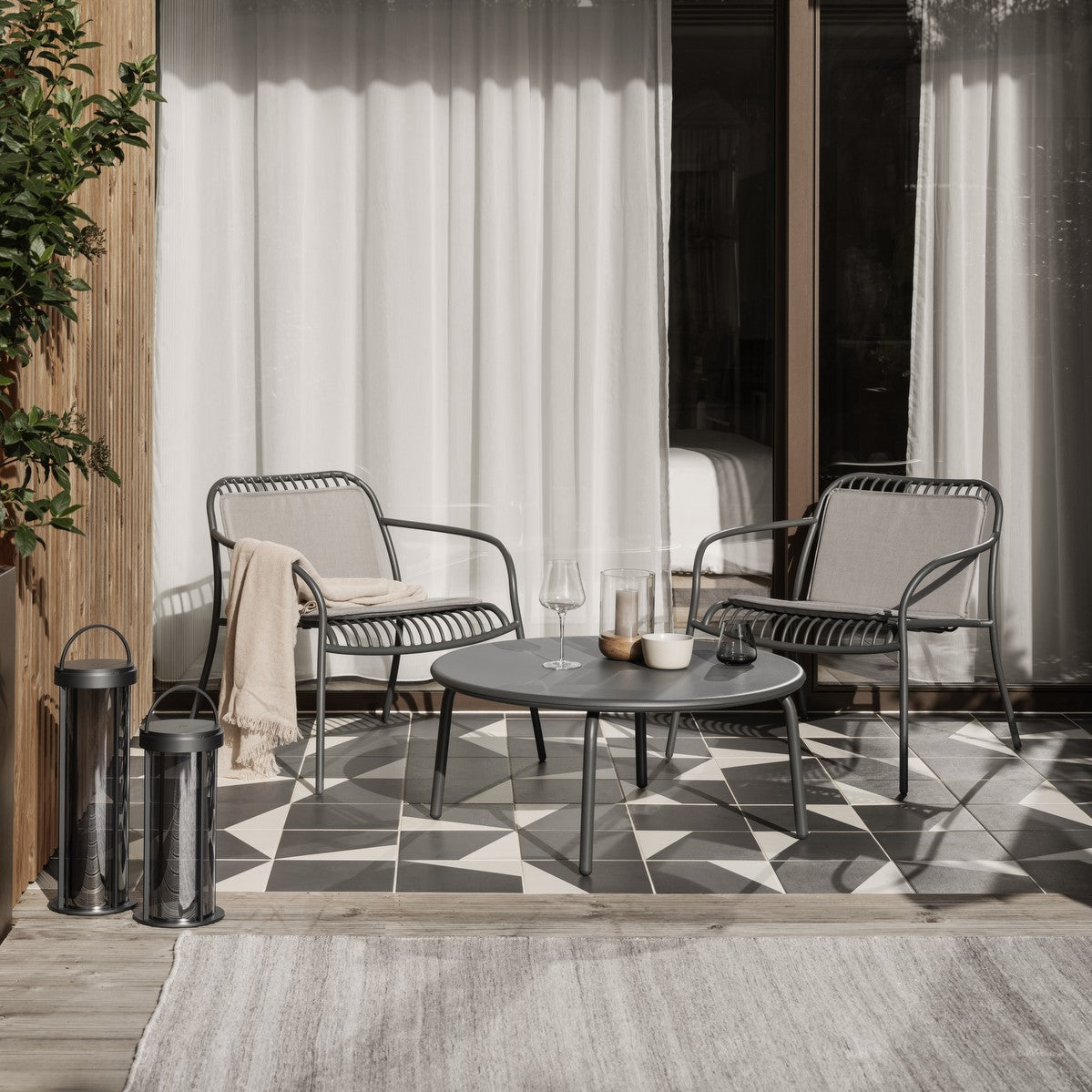 Hip outdoor patio with tile and wood flooring covered partially by outdoor reversible rug, seating area behind with metal chairs and round coffee table