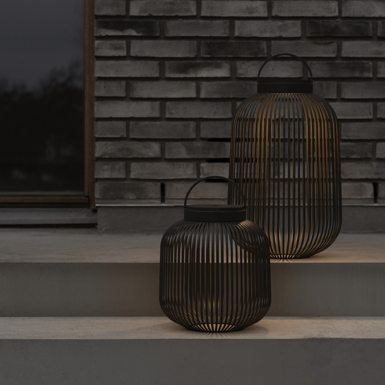 Metal wire lanterns with warm glow lighting concrete patio steps in front of brick exterior wall