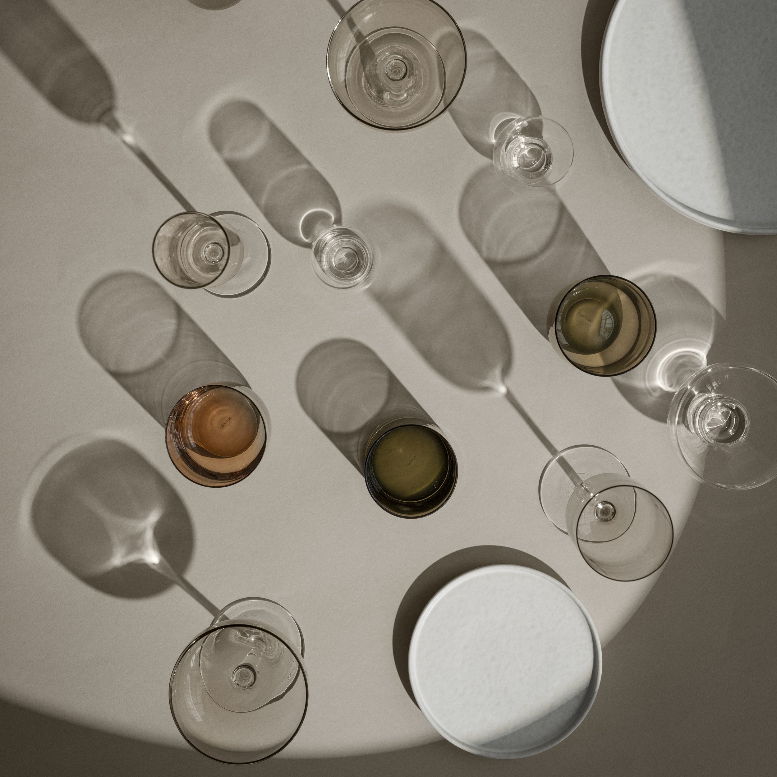 Wine glasses and bottles arranged on a reflective surface with soft shadows.