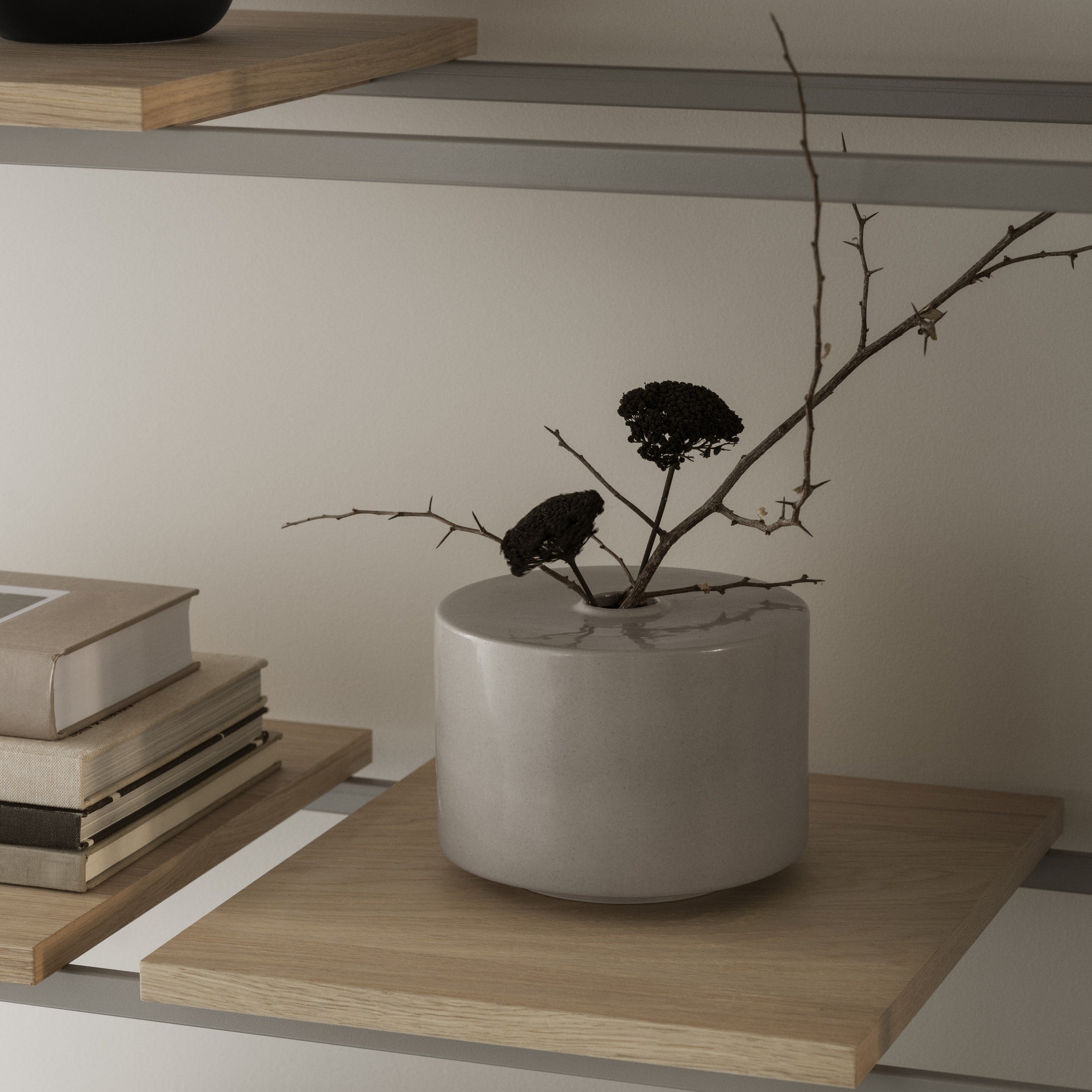 Cylindrical white vase with branches on a wooden shelf against a neutral wall.