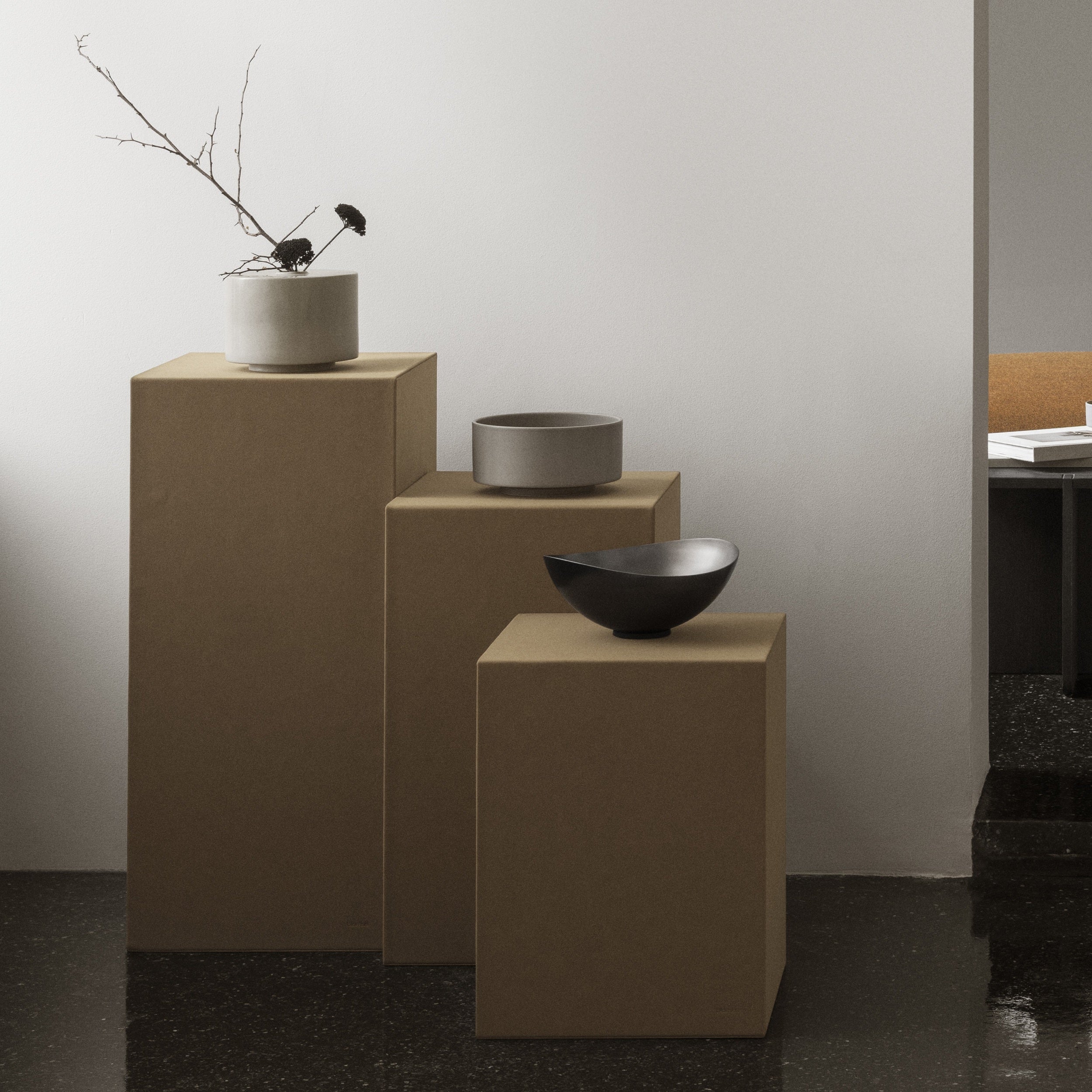 Three ceramic bowls on beige pedestals against a plain wall.