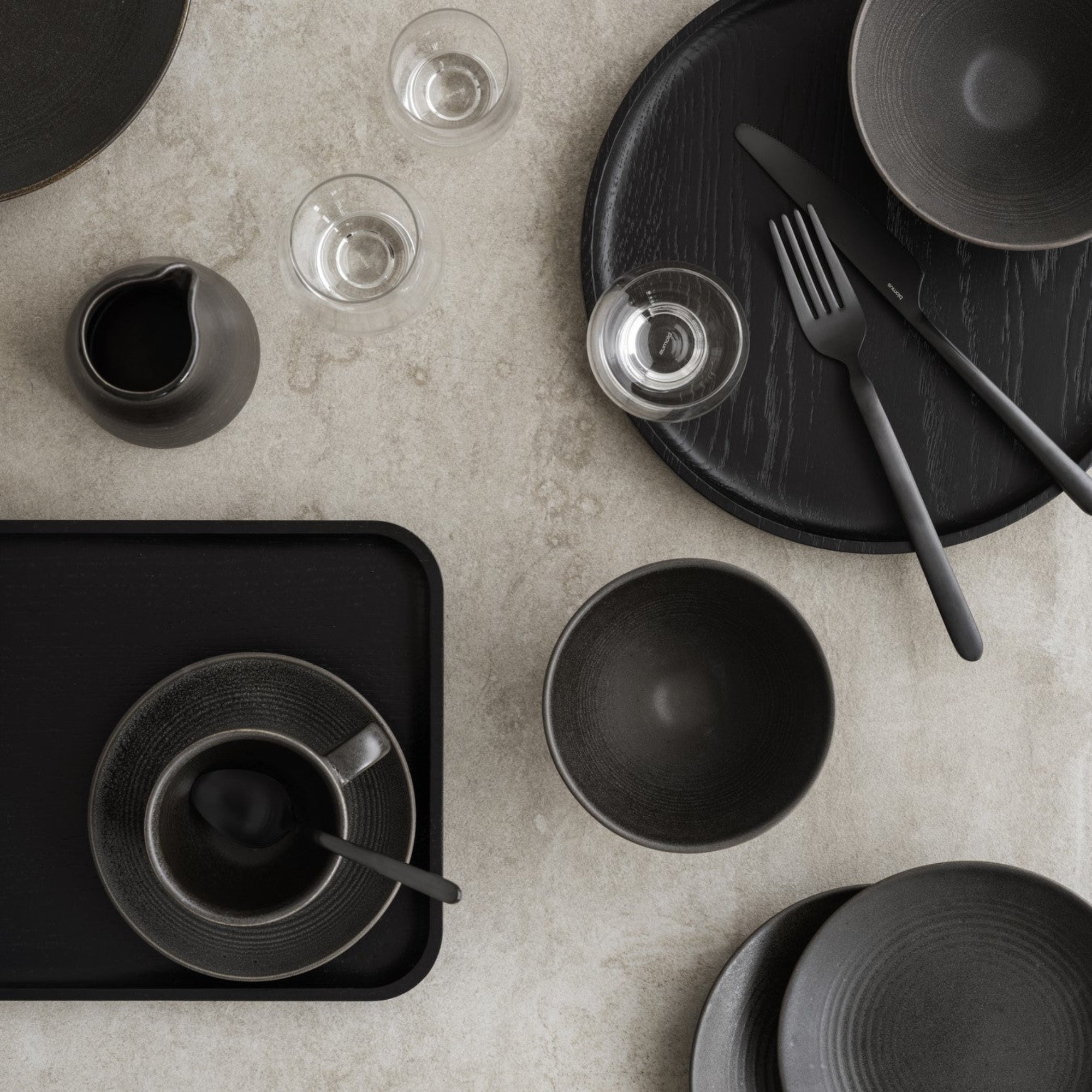 elegant dishware and black wood serving trays on natural stone surface