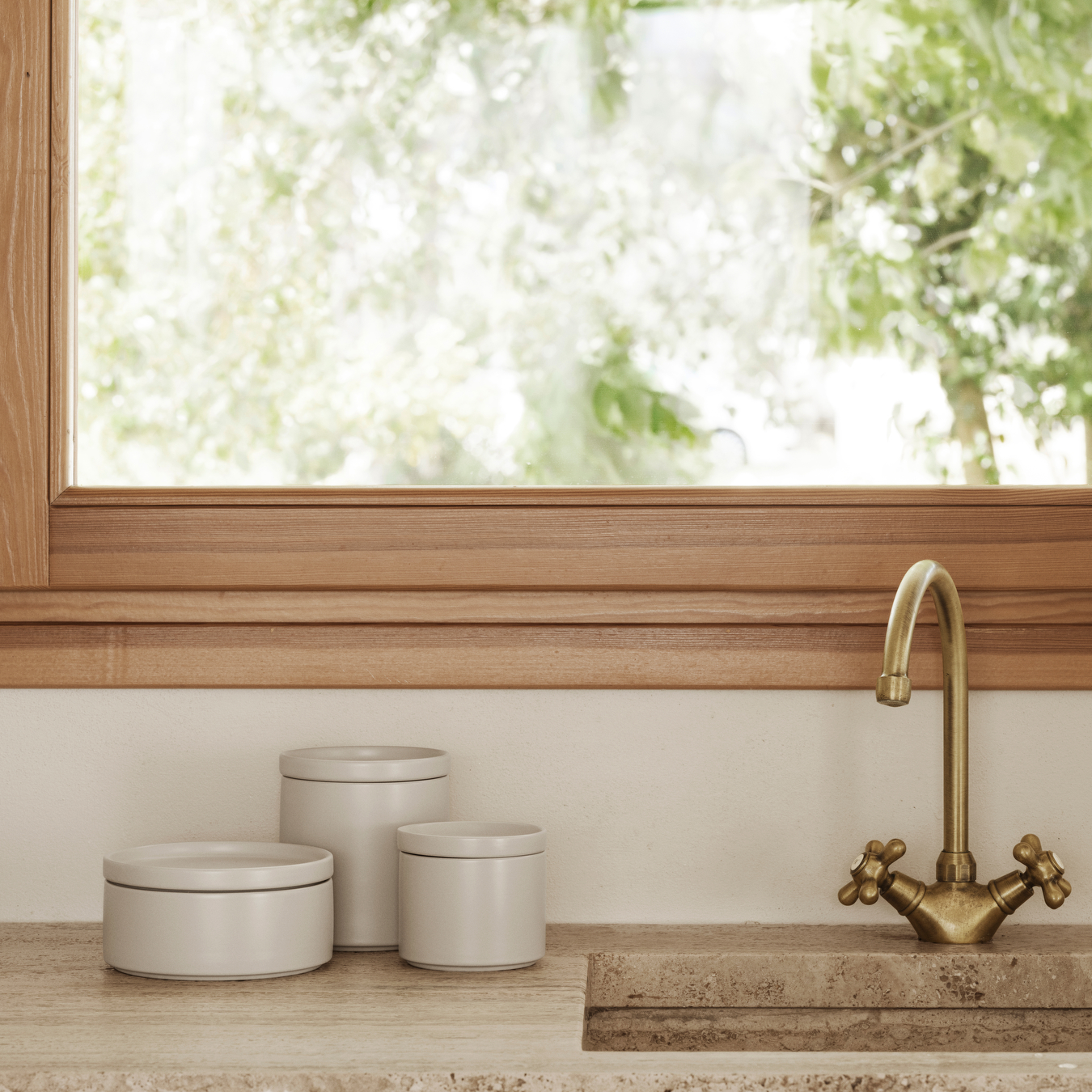 Kitchen sink area with gold faucet and PILAR Ceramic Canisters in Moonbeam canisters near a window.