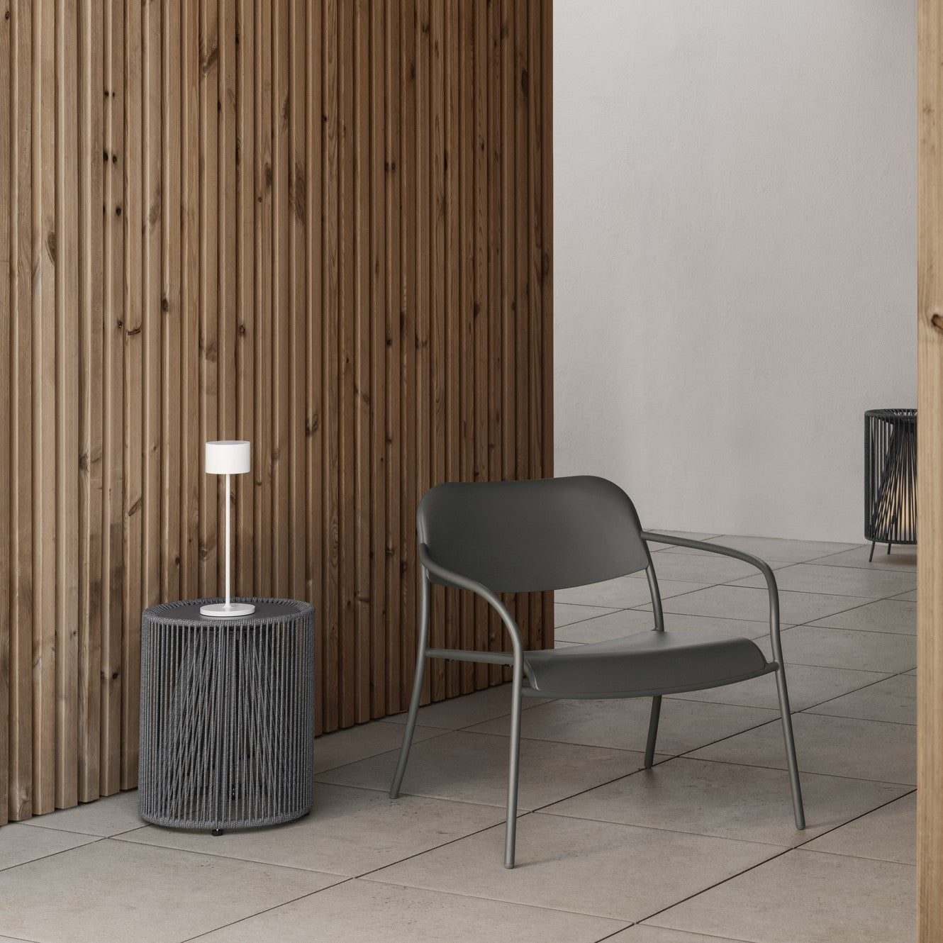 Outdoor side table with vertical rope sides next to a metal chair in a minimalist seating area