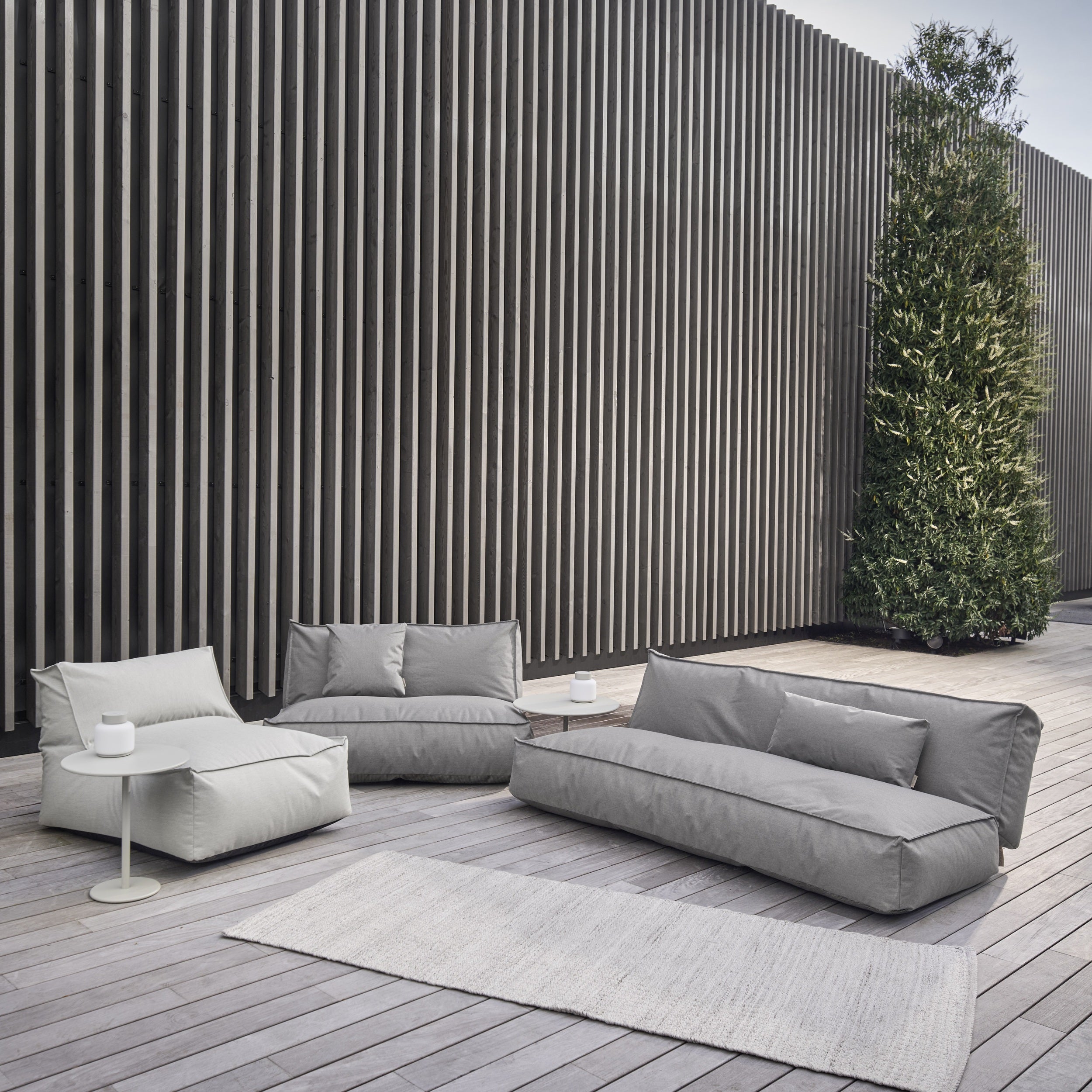 Modern outdoor furniture set on a wooden deck with a striped wall and tree in the background.