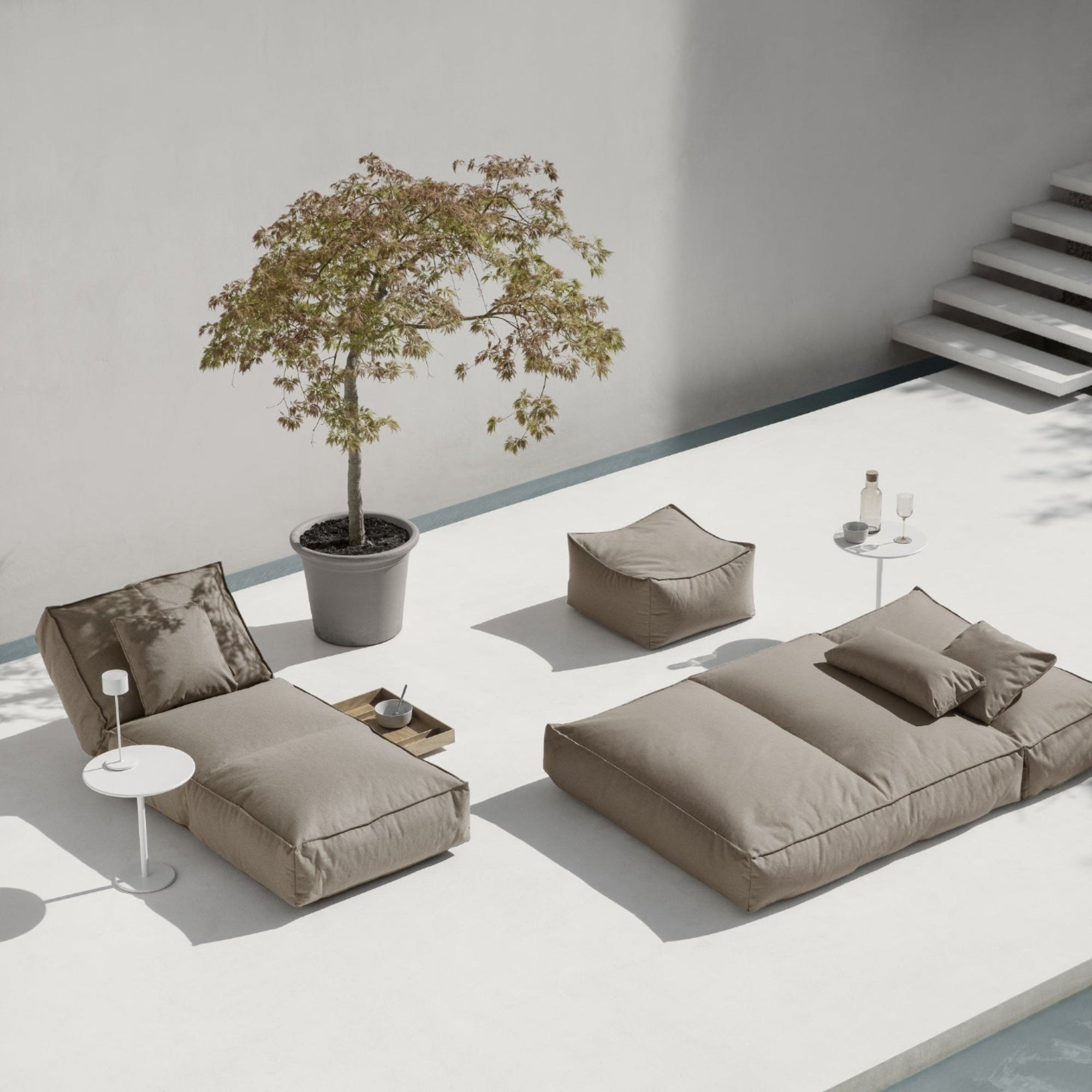 Elegant outdoor lounge area with comfy cushions next to a potted tree on a pool deck