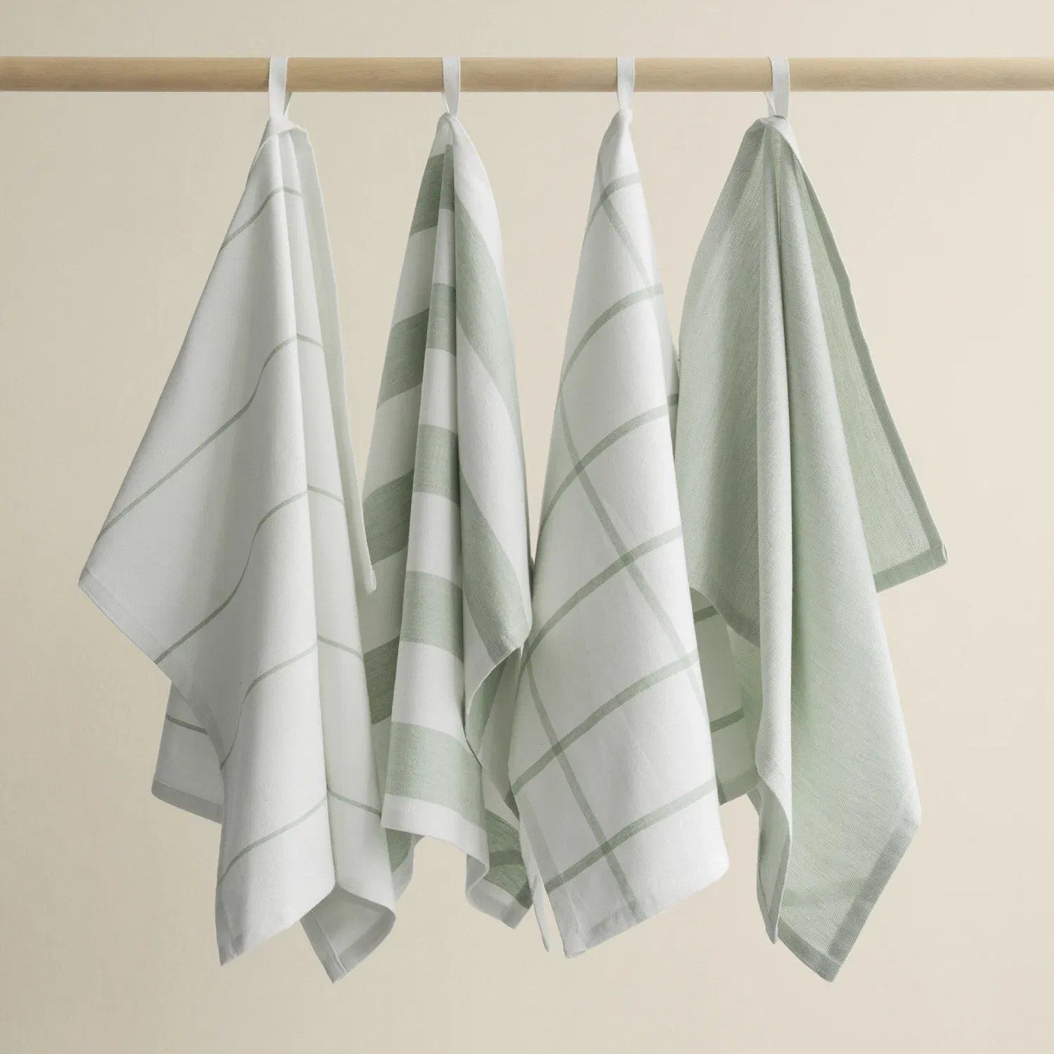 Four sage and white patterned towels hanging on a rack against a beige background
