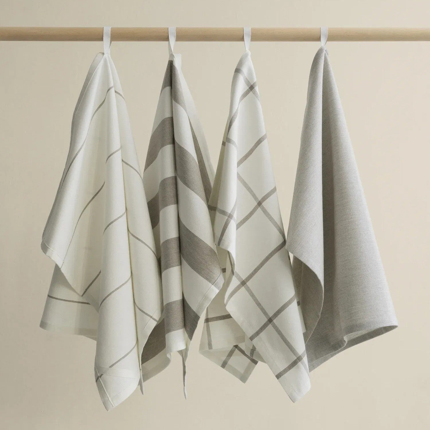Four TAULO Tea Towls towels hanging on a rod against a beige background