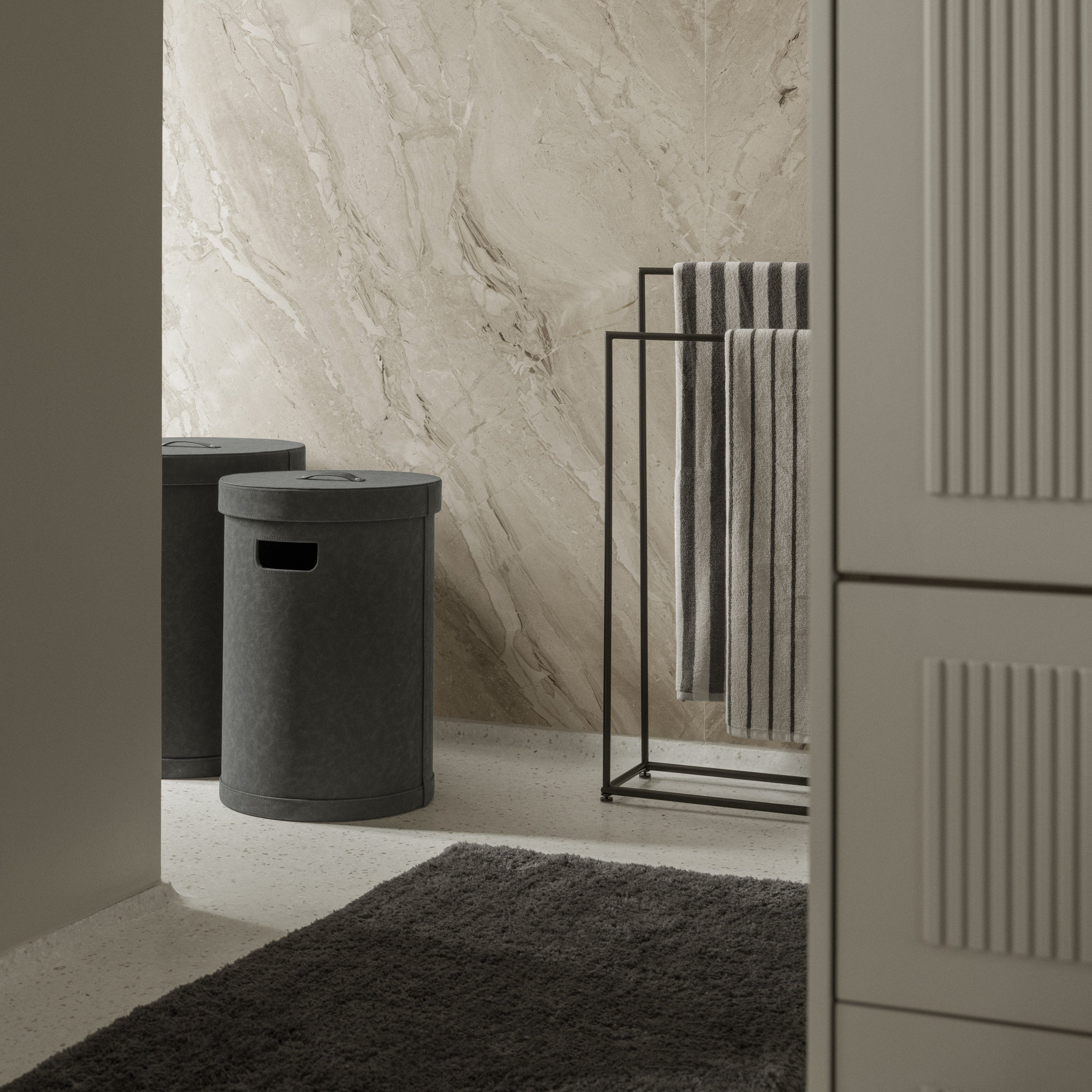 Bathroom interior with a bath mat, towel rack, storage bins, and a textured wall.