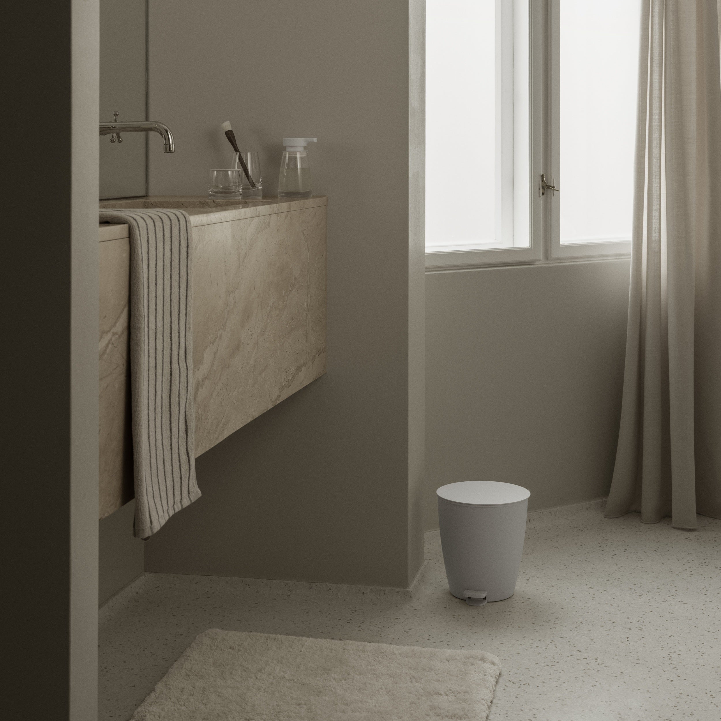 Bathroom with a bath mat, towel, and trash can on a light gray floor.