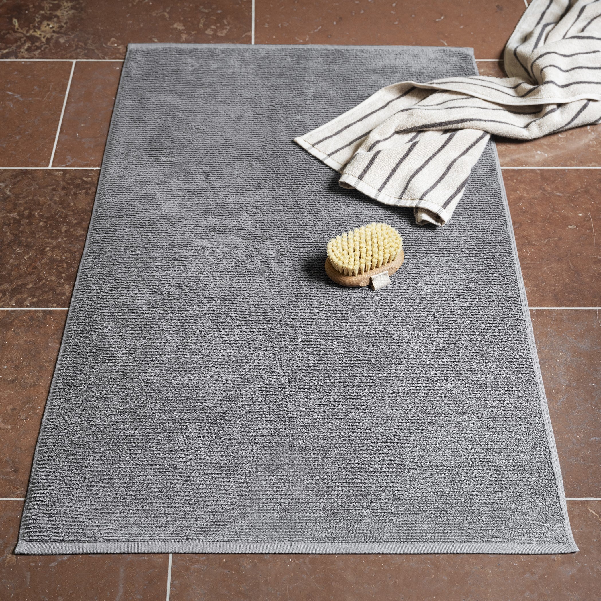 TUYO Bathmat sitting on tile floor with towel and bathing brush.