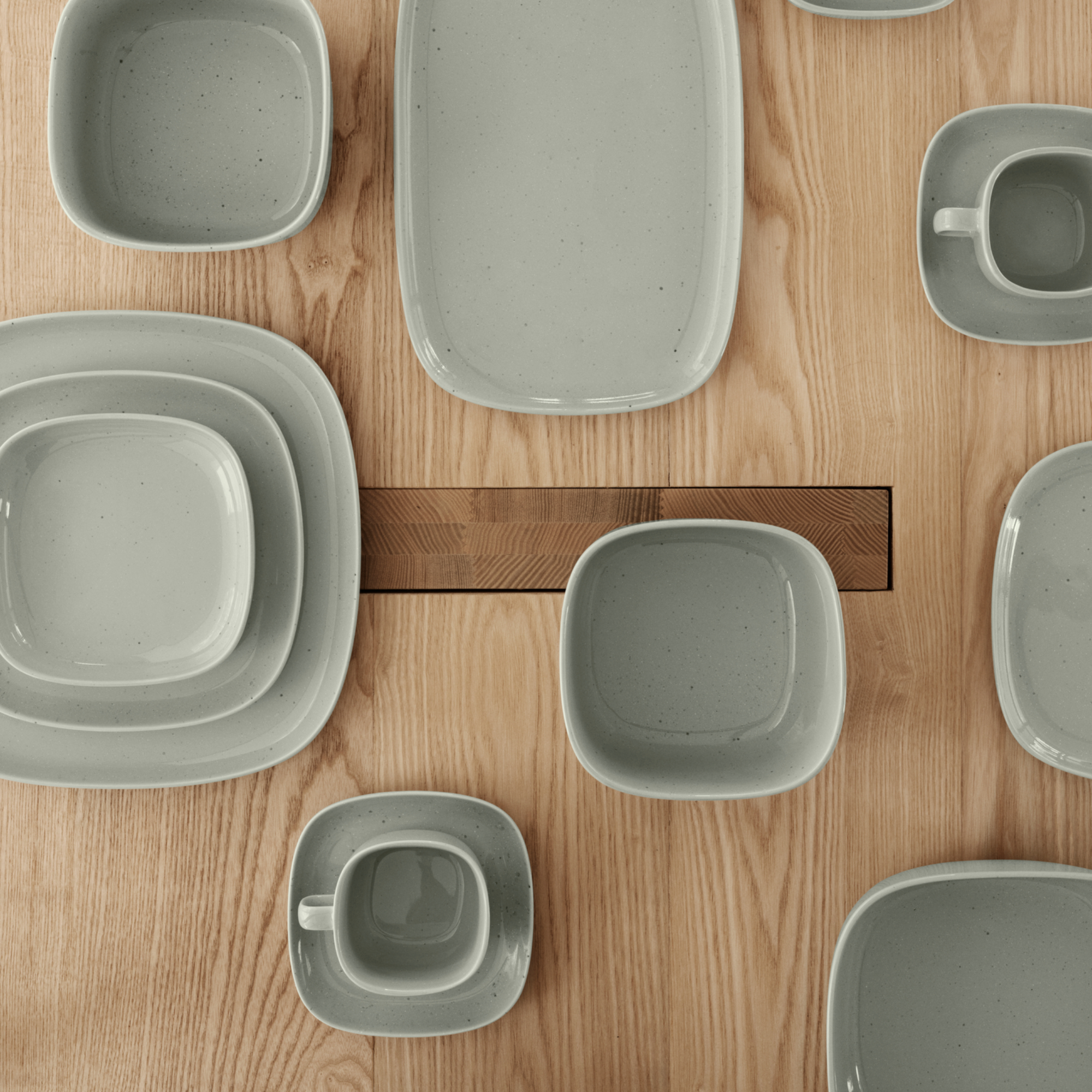 A wood table set with VAHLO Mirage Grey dishes with the picture taken from above looking down on the dishes and table.