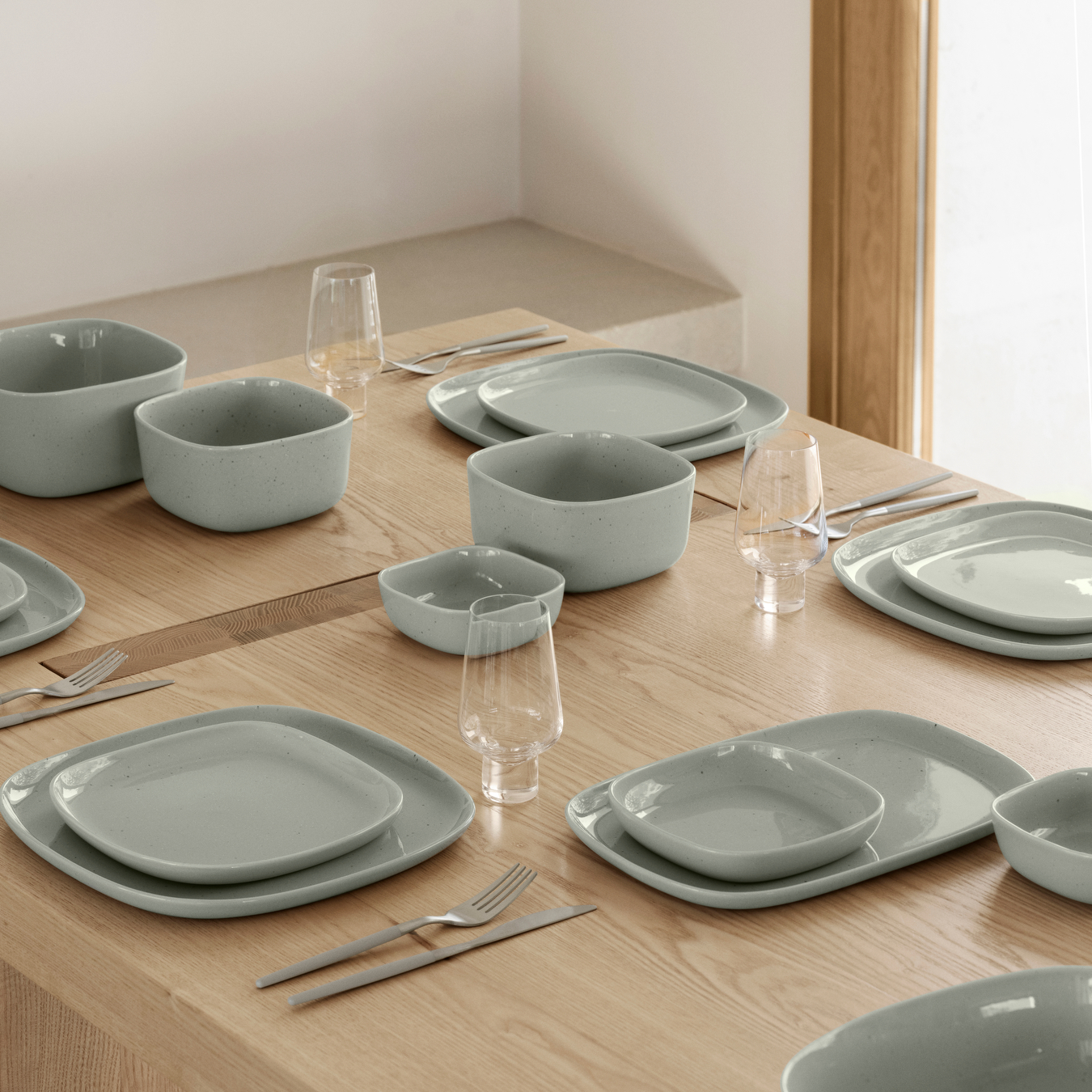 A wood table set with VAHLO Dishes including bowls, plates, serving trays in Mirage Grey and KOYOI Glasses in a neutral colored room.