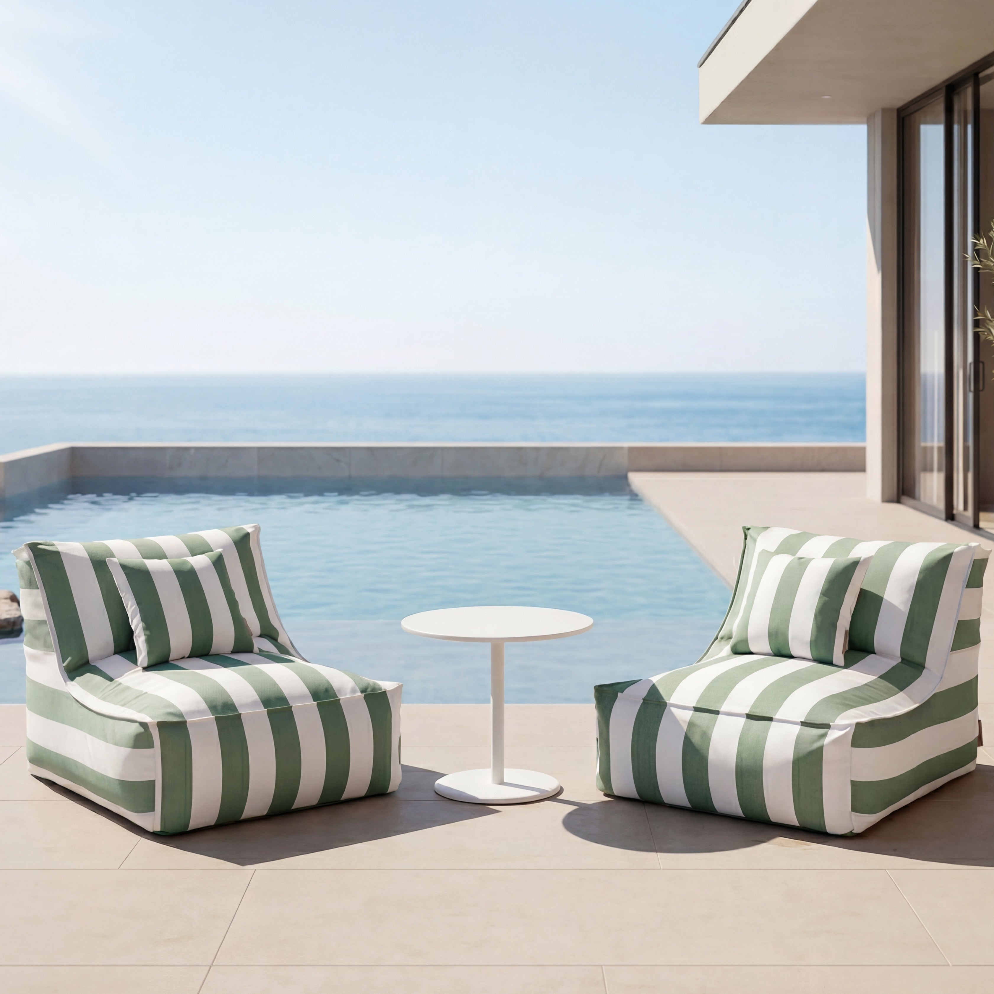 Two green and white striped chairs with a small table on a patio overlooking the ocean.