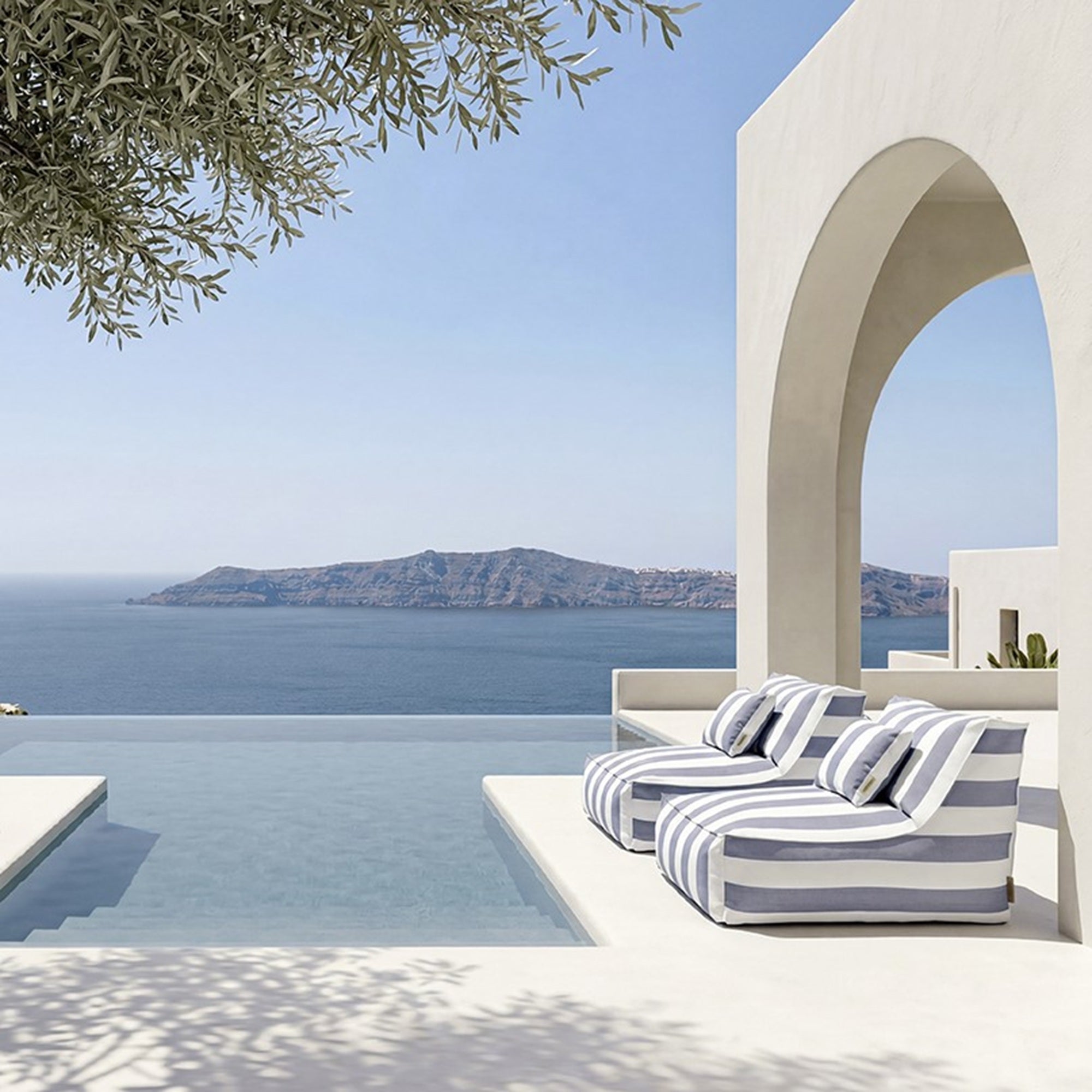Striped lounge chairs by a pool with a scenic ocean view and white archway.