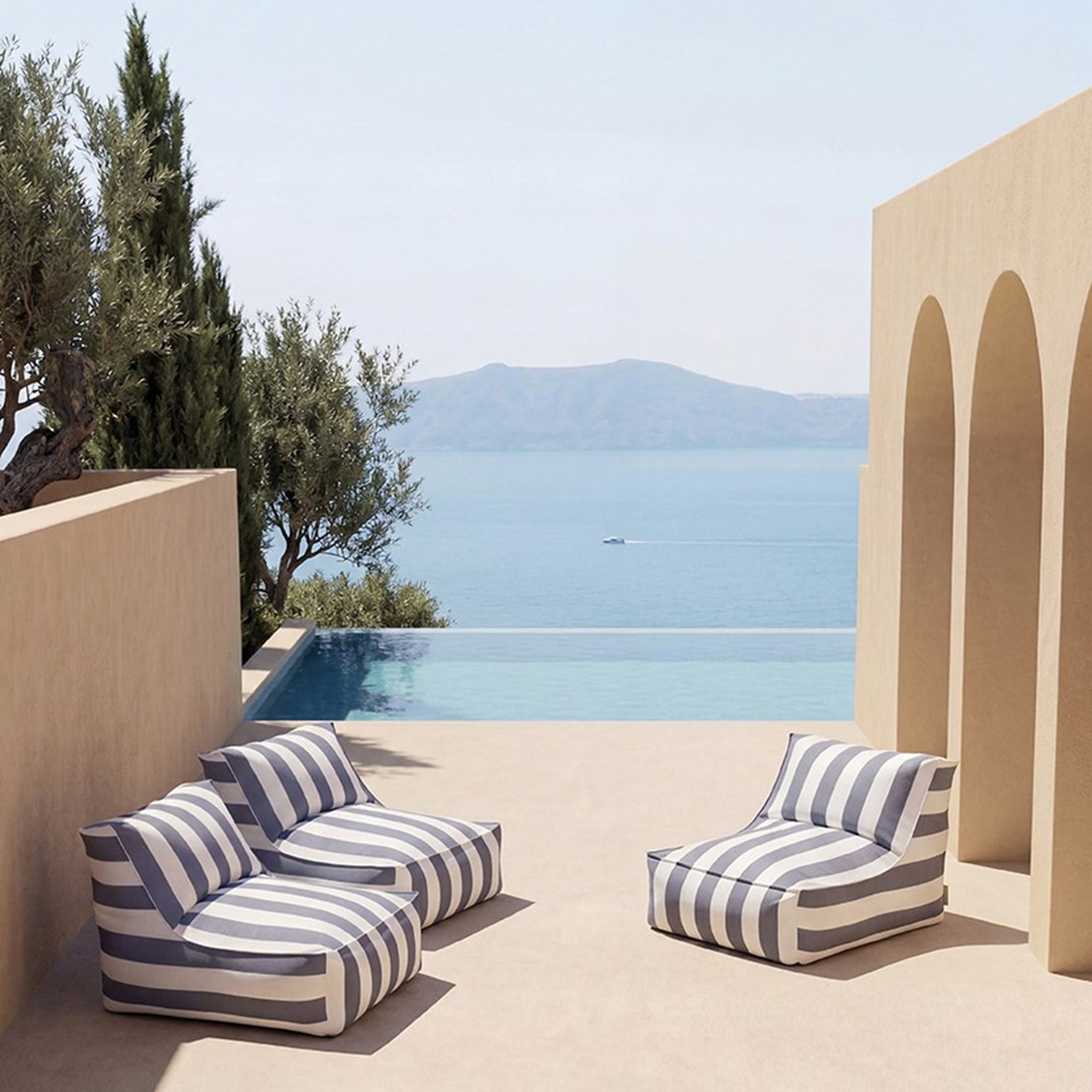 Striped outdoor chairs by a pool with a scenic view of mountains and sea.