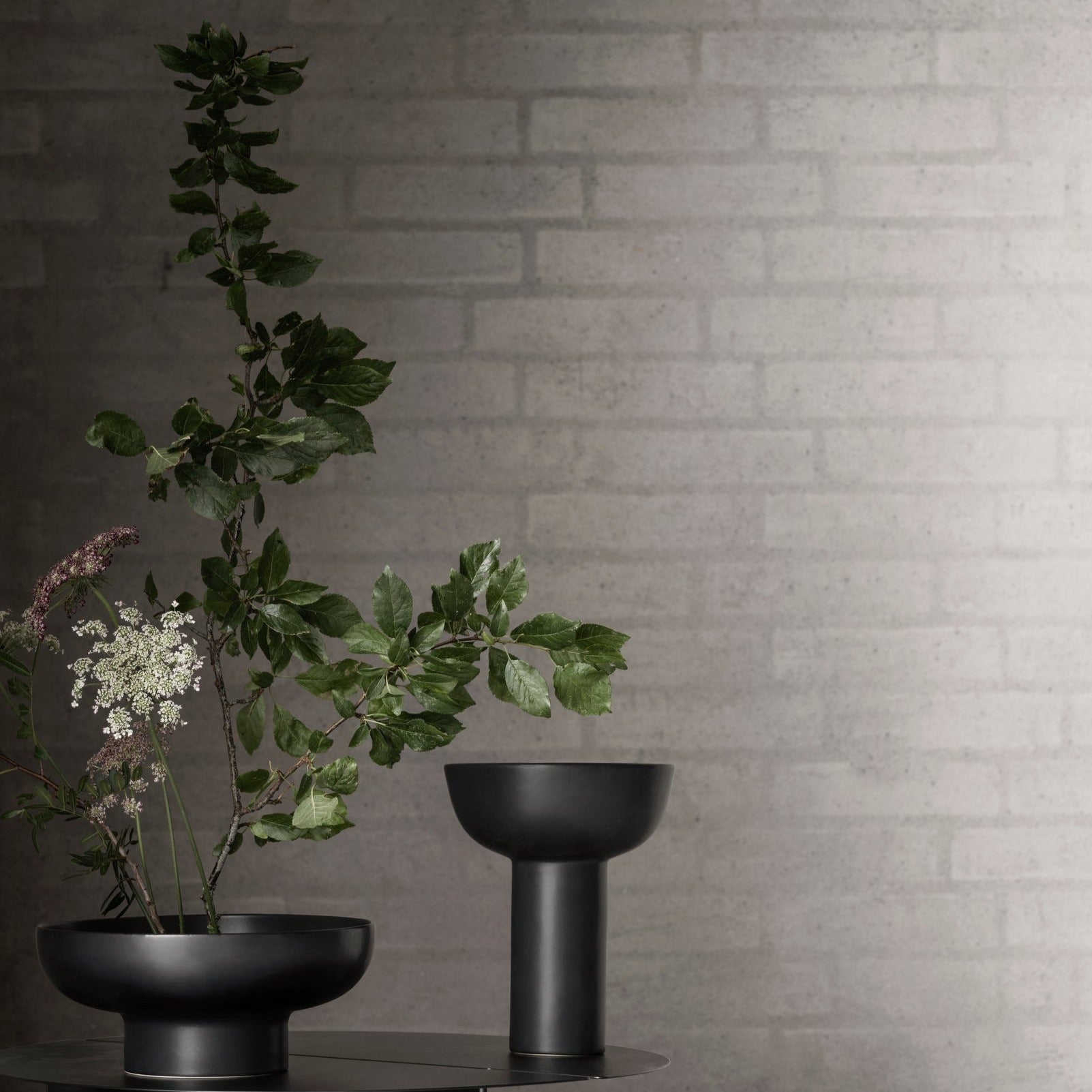 blomus MIYABI vases with arrangement of wildflowers in a dimly lit room against painted brick wall