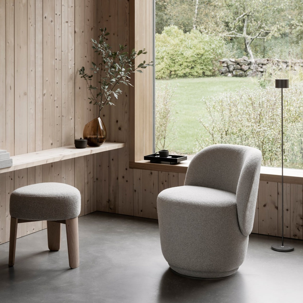 Modern sitting area near a window with views of lush greenery, comfy chair next to the window with tall floor lamp for reading