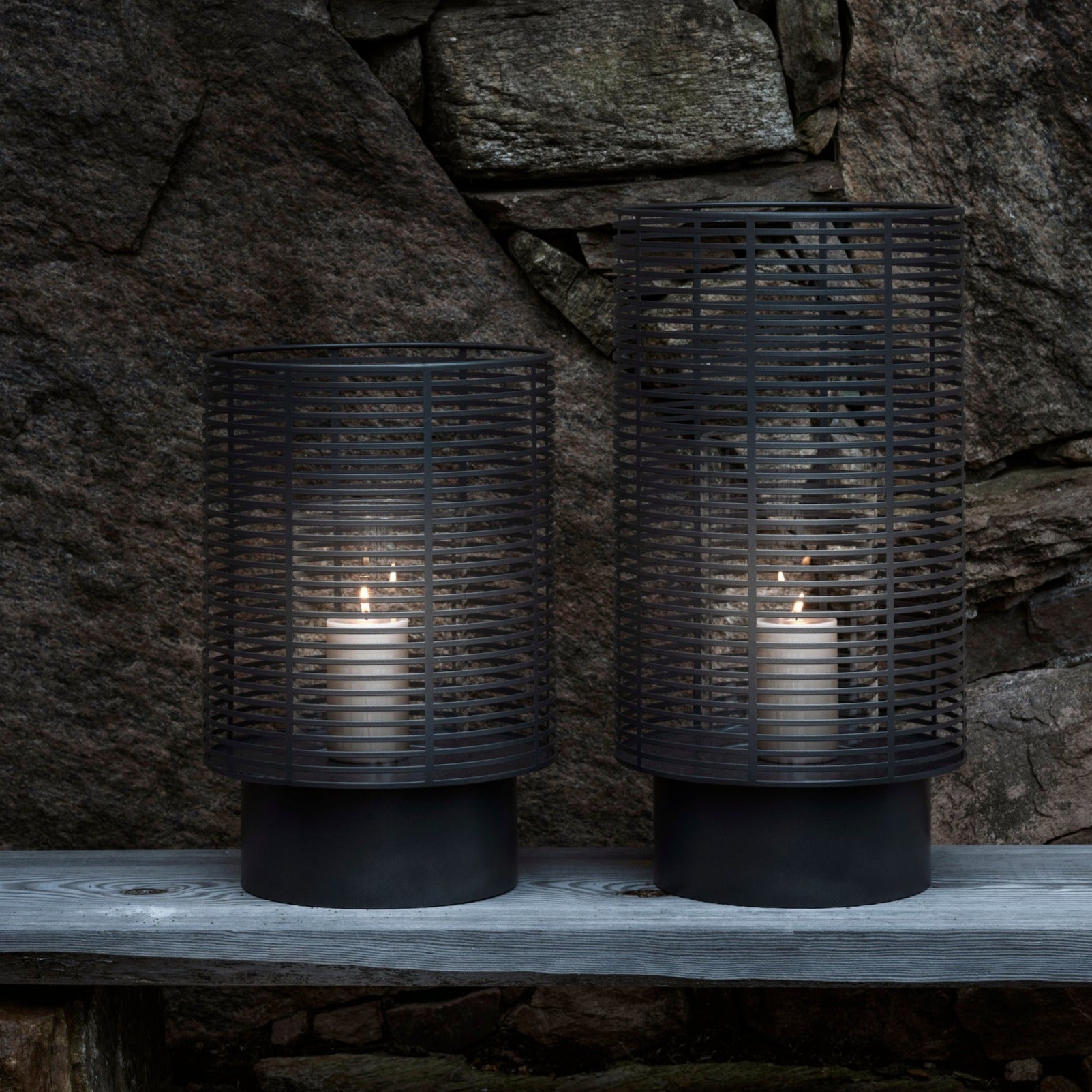 Metal outdoor lanterns with candles burning next to stone wall