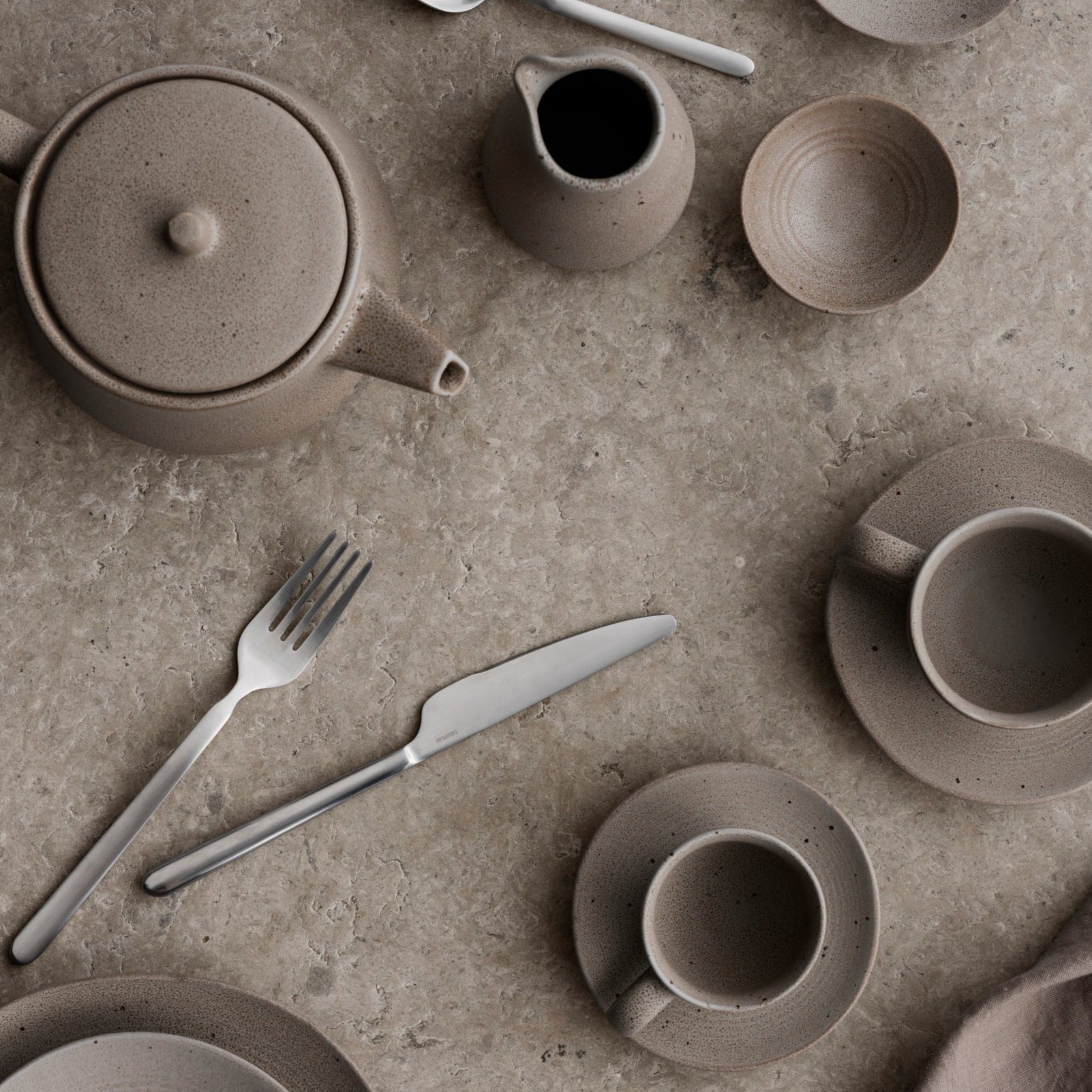 blomus KUMI ceramic glazed tableware coffee cups and cream and sugar containers on a textured stone surface
