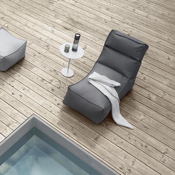 Poolside lounger with white outdoor side table on a wooden deck