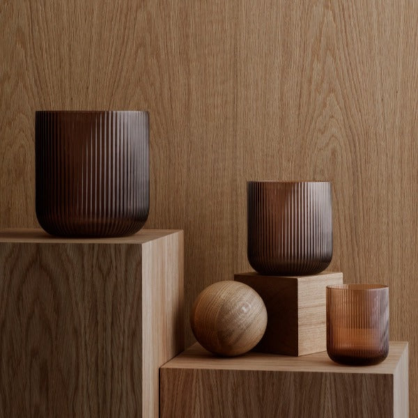 Coffee colored VEN hurricane lamps displayed on blocks of wood with exposed grain