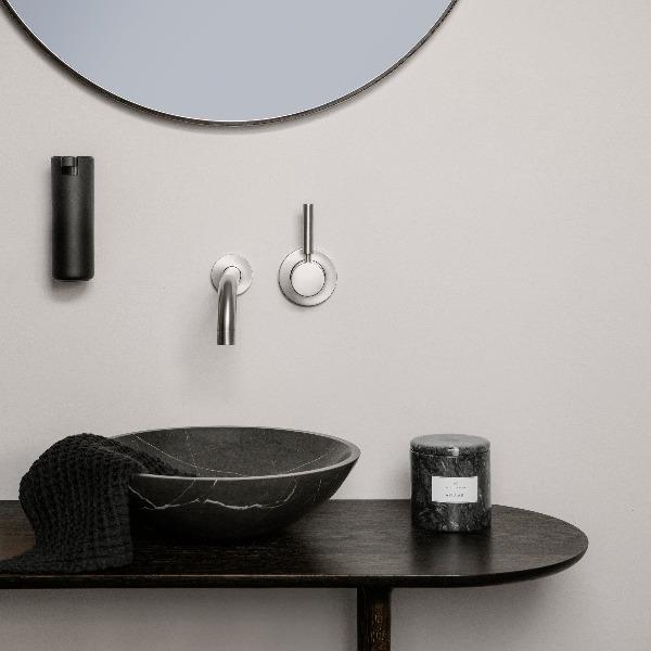 wall mounted soap dispenser with sleek black metal finish above a marble sink in a modern bathroom
