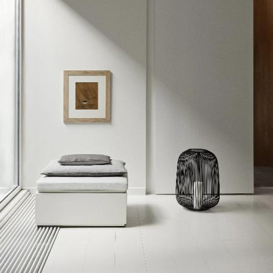 blomus LITO floor lantern next to an ottoman in a minimalist home decor setting