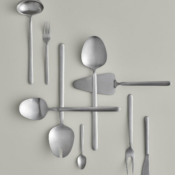 assortment of blomus STELLA brushed stainless utensils arranged in a minimalist fashion against  light grey background