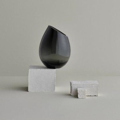 DROP smoked glass vase by blomus precariously perched upon industrial blocks against a plain backdrop
