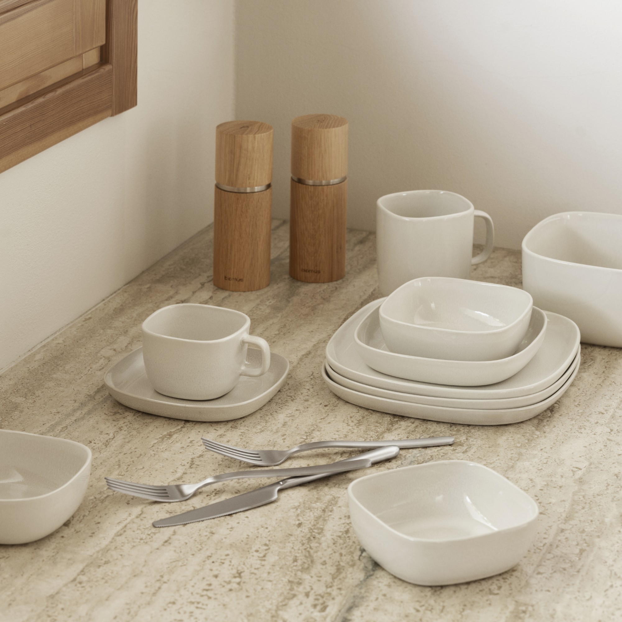 VAHLO Moonbeam Plates, Bowls and Coffee Cups placed on a neutral colored counter with silverware and salt and pepper grinders.