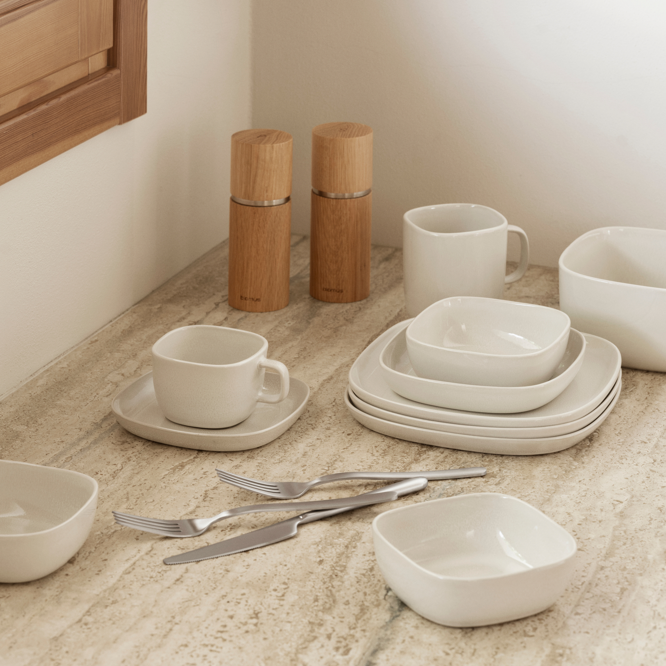 VAHLO Moonbeam Plates, Bowls and Coffee Cups placed on a neutral colored counter with silverware and salt and pepper grinders.