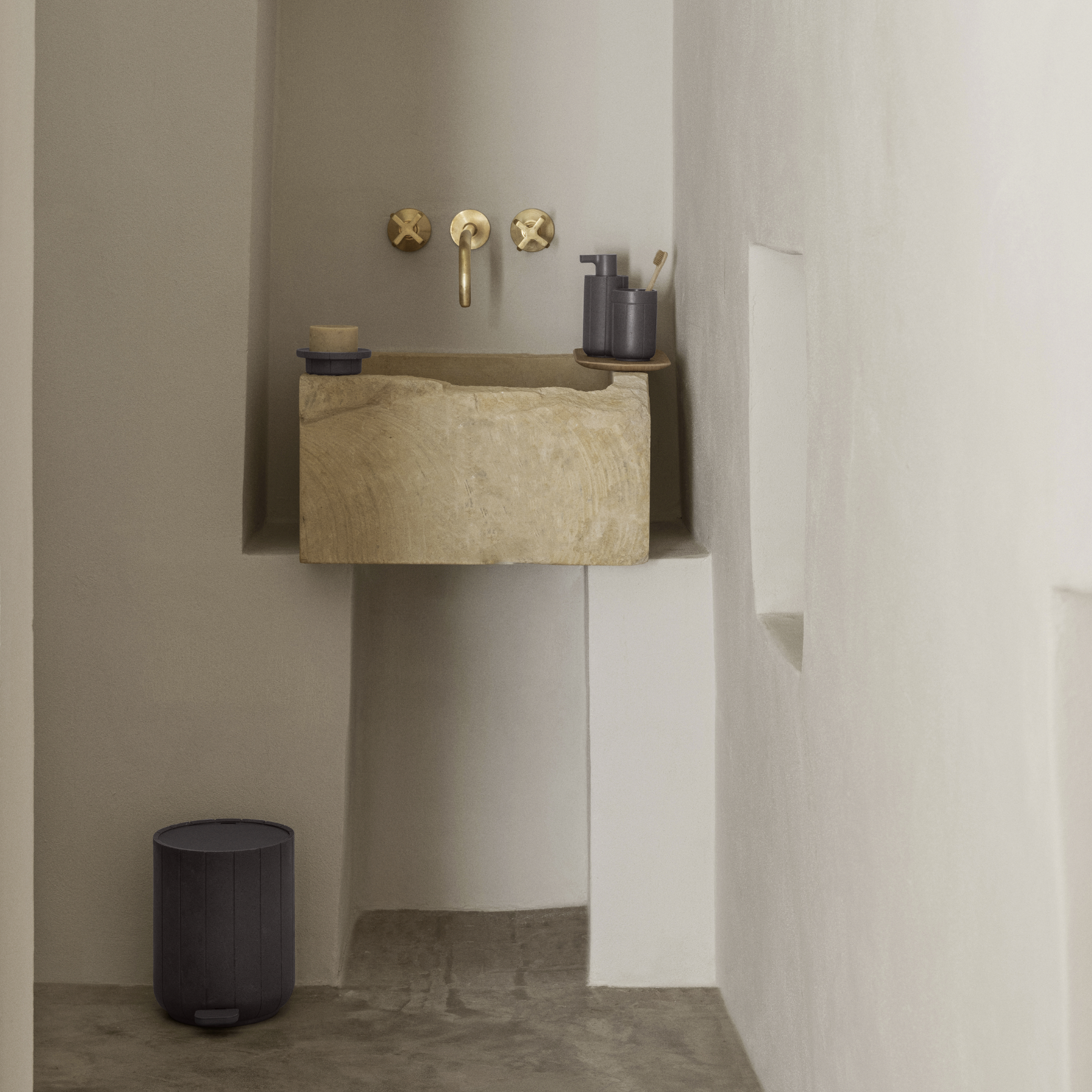 blomus KUA Soap Dispenser, Tray, Tumbler and Wastebasket shown on a bathroom sink with gold fixtures against a neutral wall. Soap Dispenser and Tumbler are placed on a BAKI Tray.