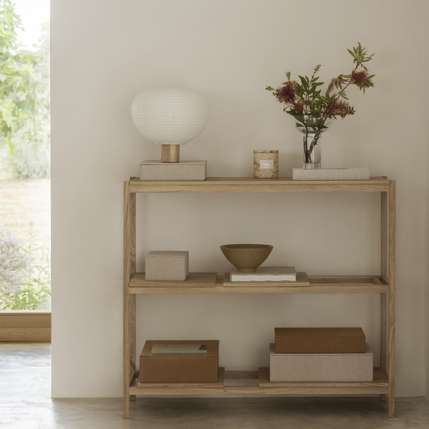 MIYABI Glass Vase containing flowers sitting on a SUKOYA Shelf with SAHLA Storage Boxes, candles, lamps, books. 