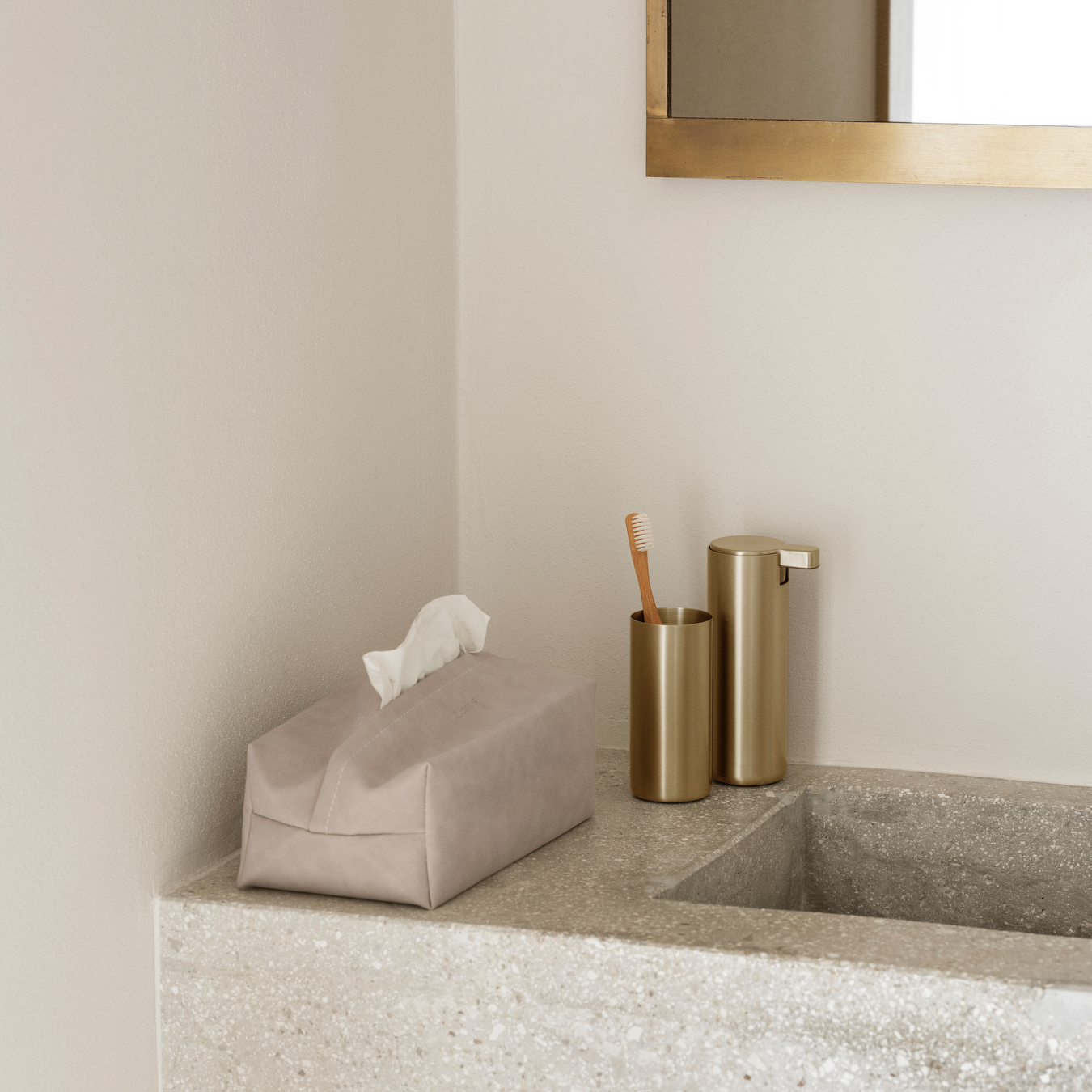 Bathroom counter with SAHLA Tissue Box Cover and blomus MODO Tumbler and Soap Dispenser in brass color against a beige wall.