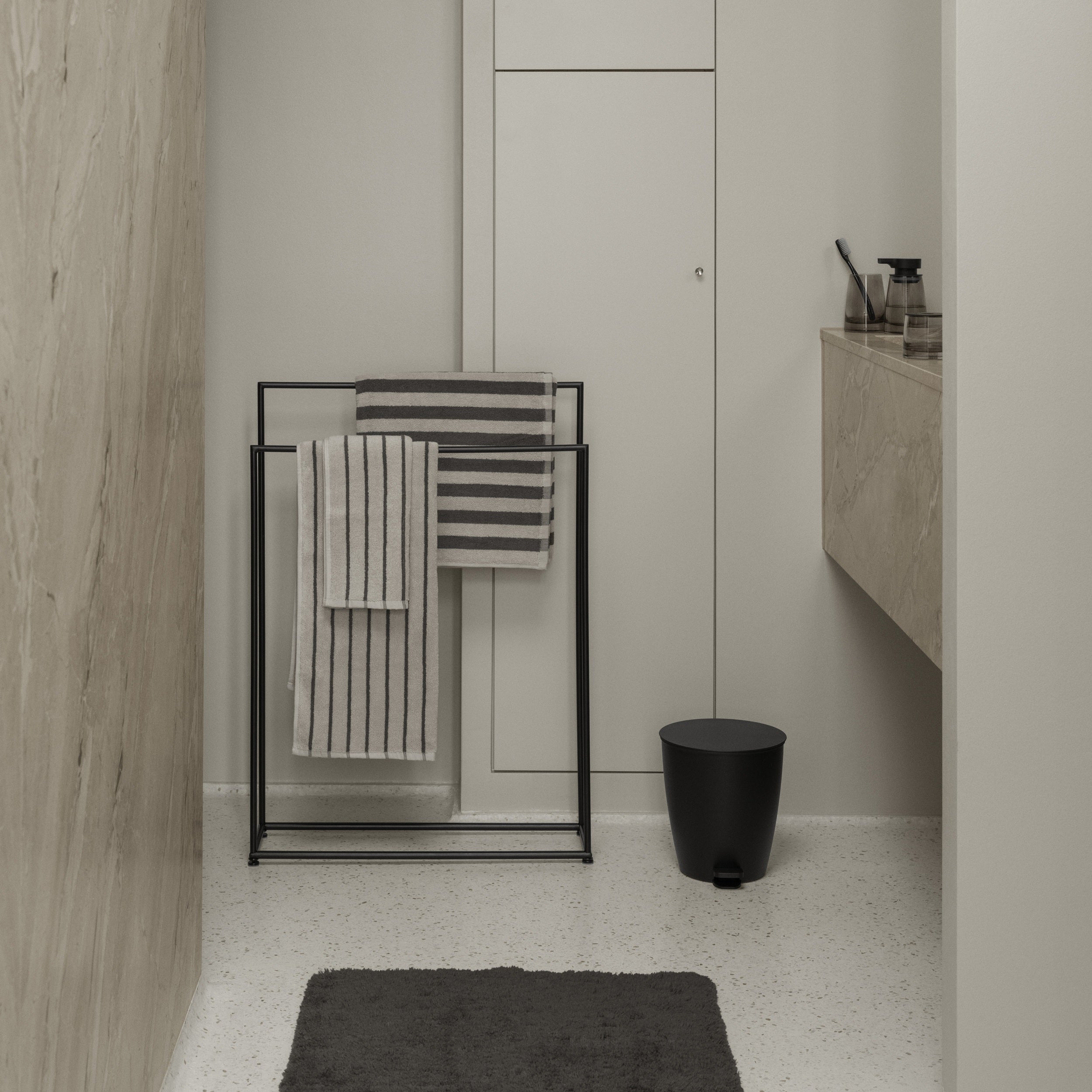 Bathroom interior with towel rack, towels, and a black trash can.
