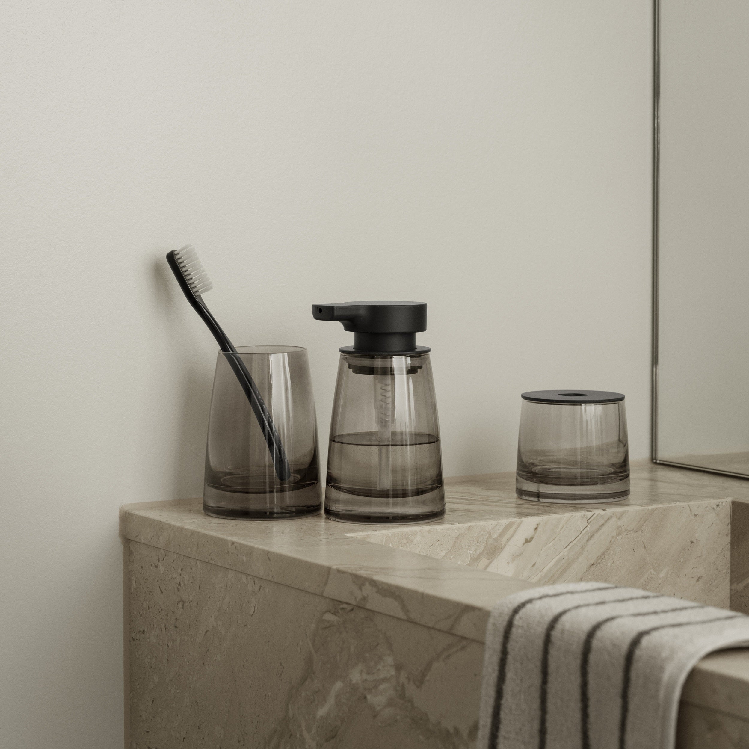 Bathroom counter with smoked glass containers, a brush, and a striped towel.