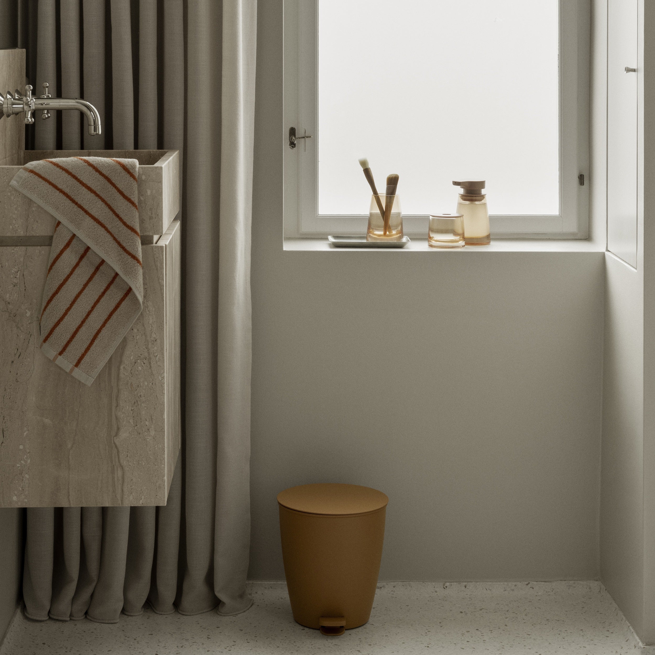 Bathroom with a sink, towel, and small stool near a window.